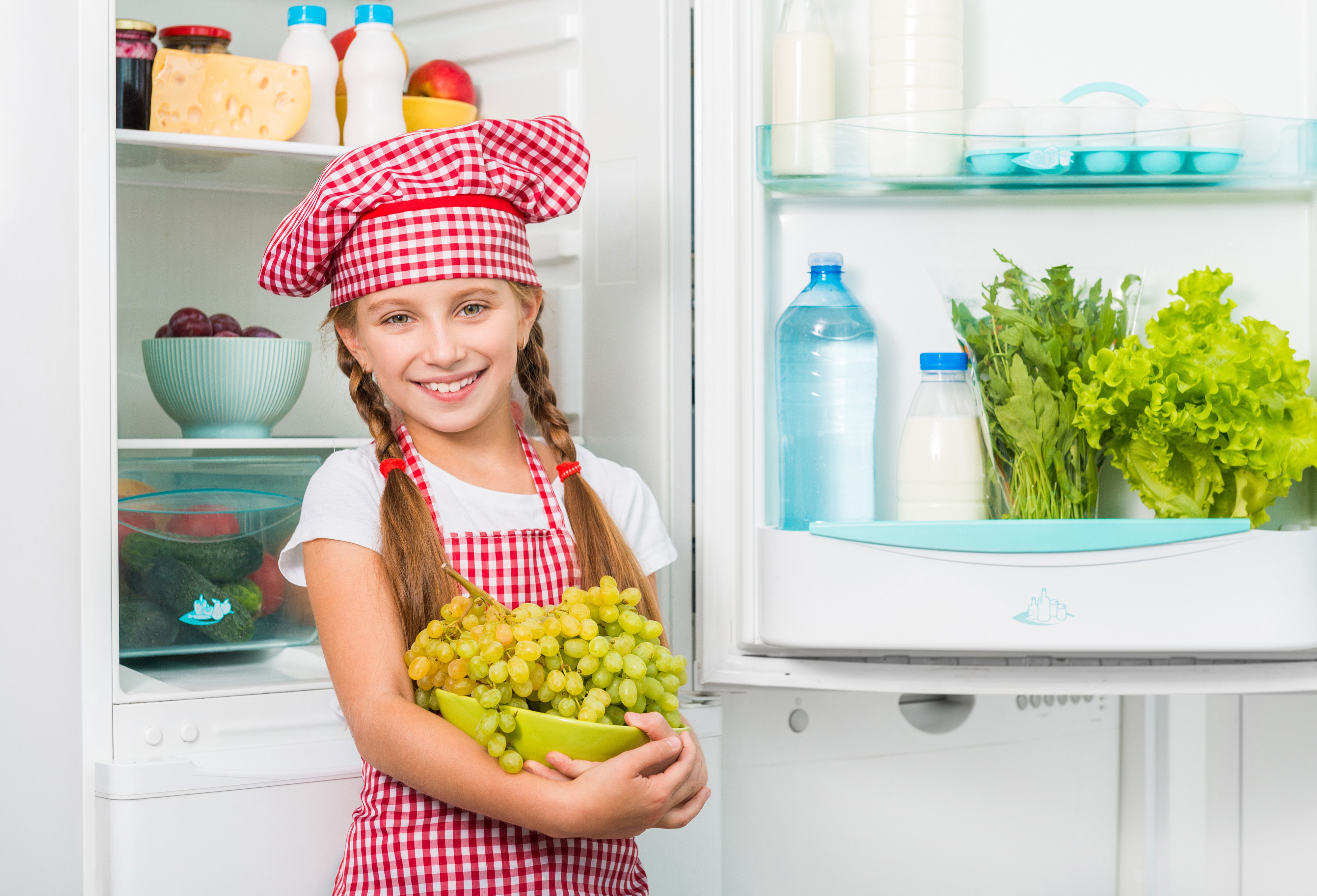 Girl in chef hat holding grapes in front of refrigerator HD Wallpaper