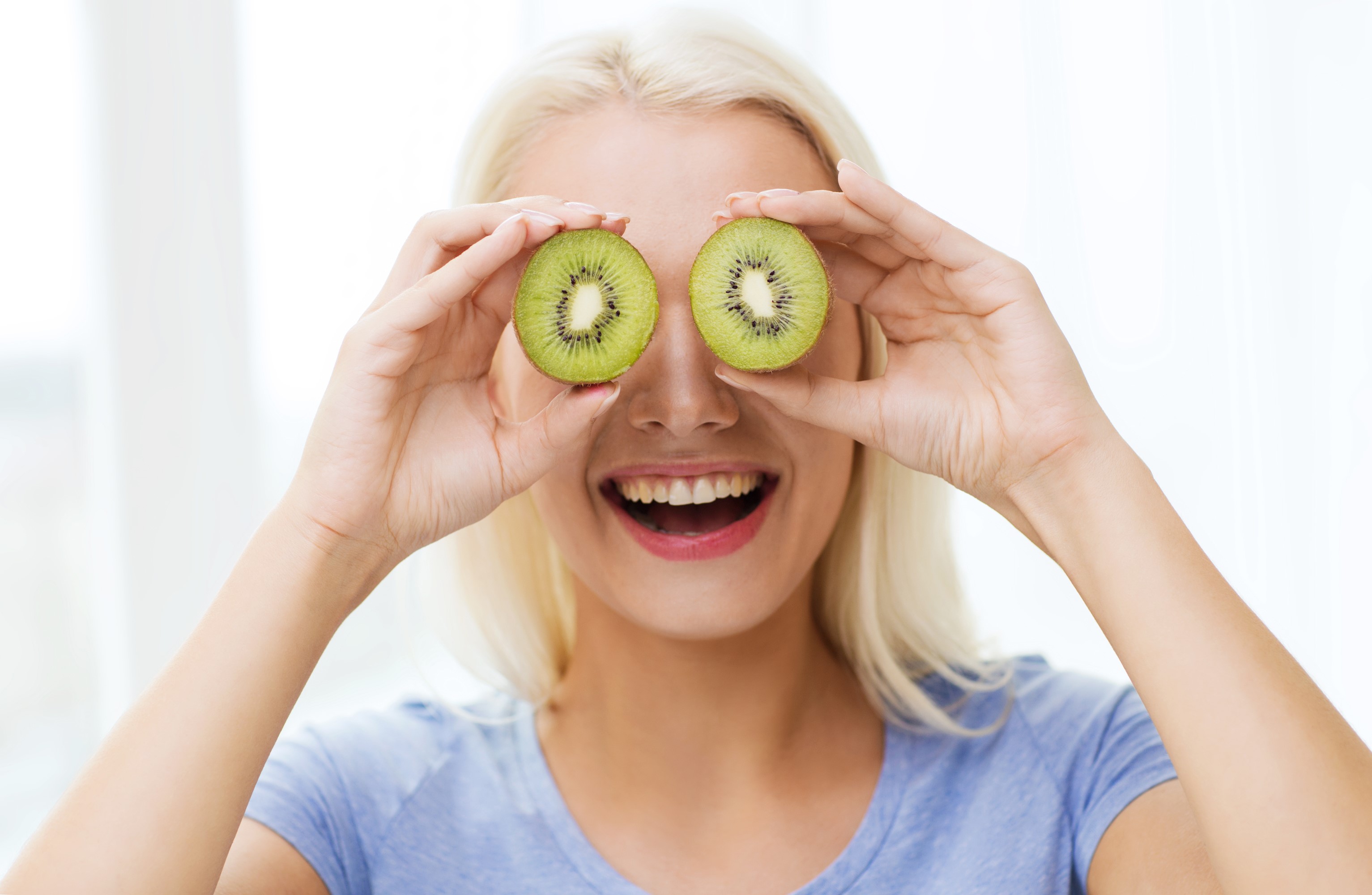 Blonde woman holding kiwi slices over her eyes HD Wallpaper
