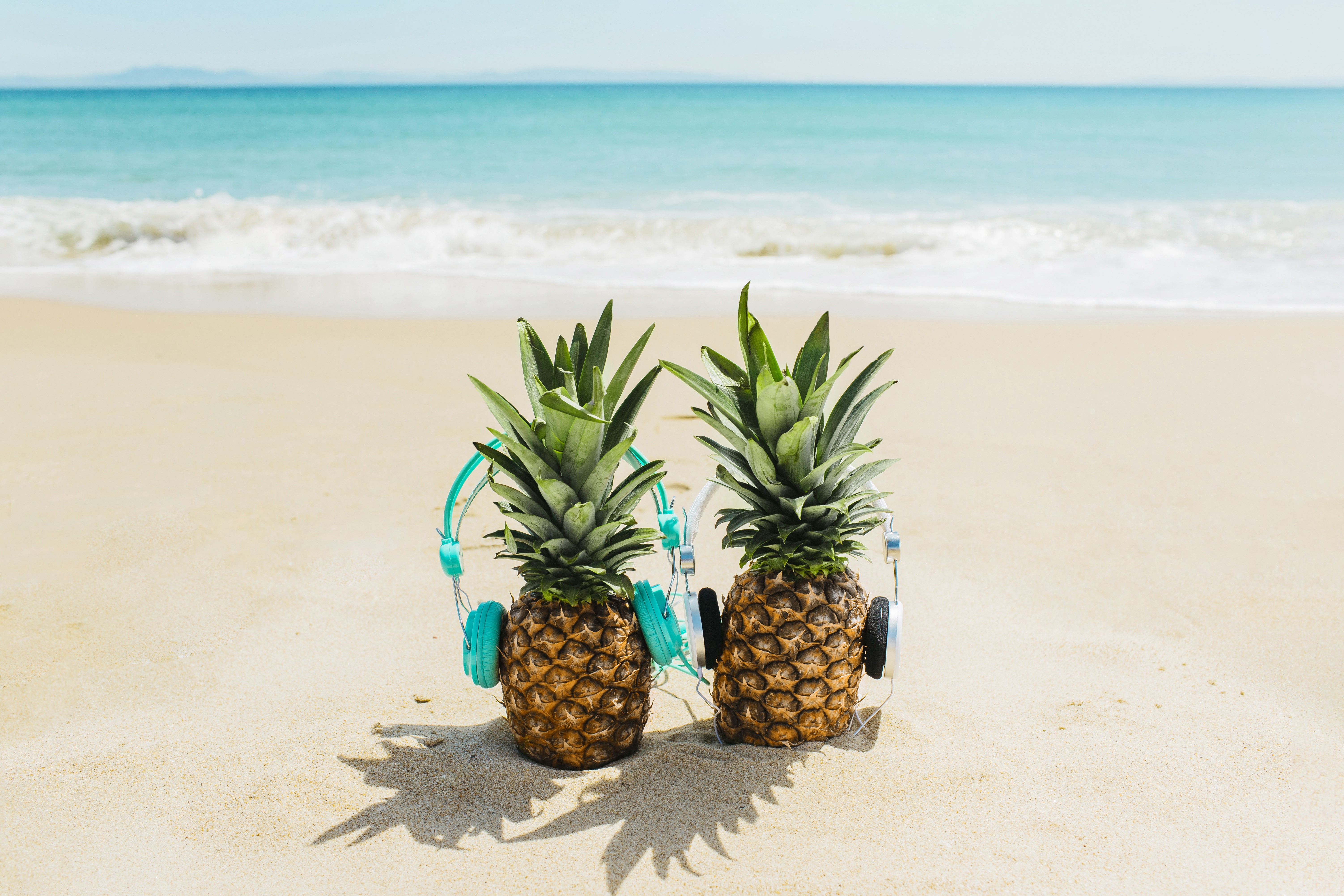 Two pineapples with headphones on a beach HD Wallpaper