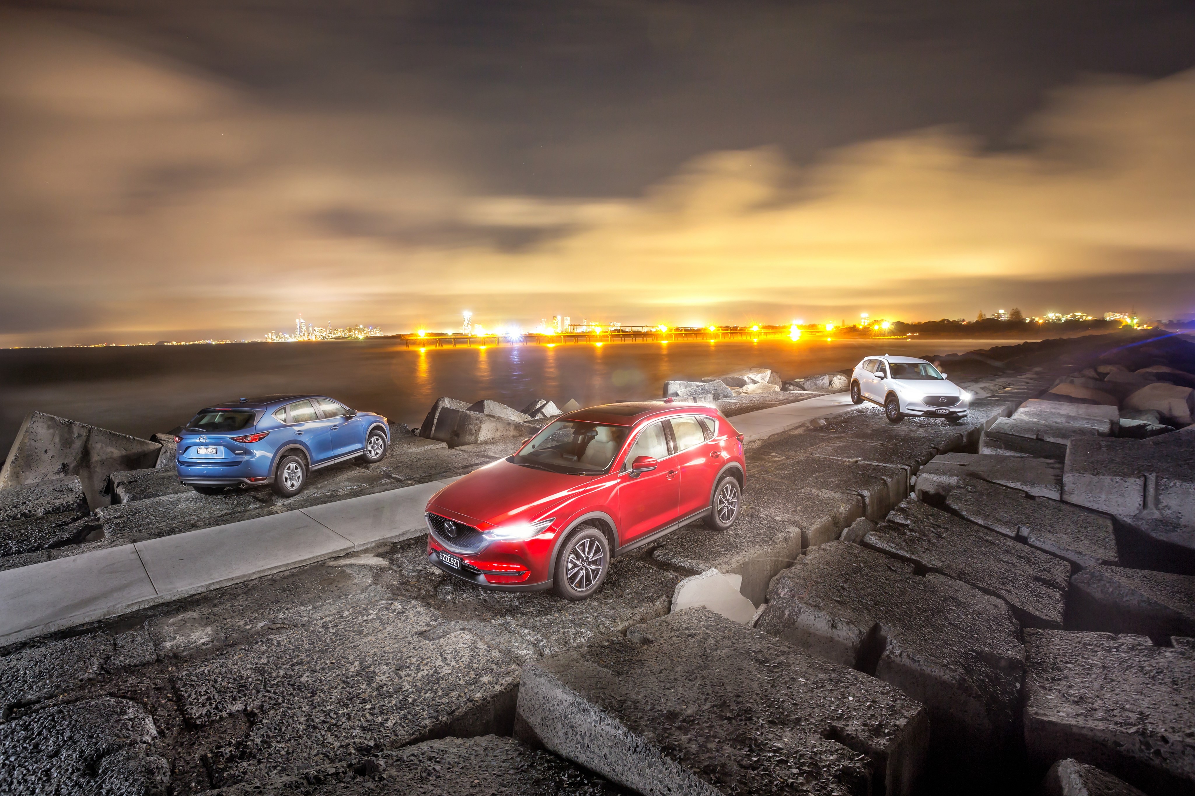 Three Mazda CX-5 SUVs on a rocky pier at night HD Wallpaper