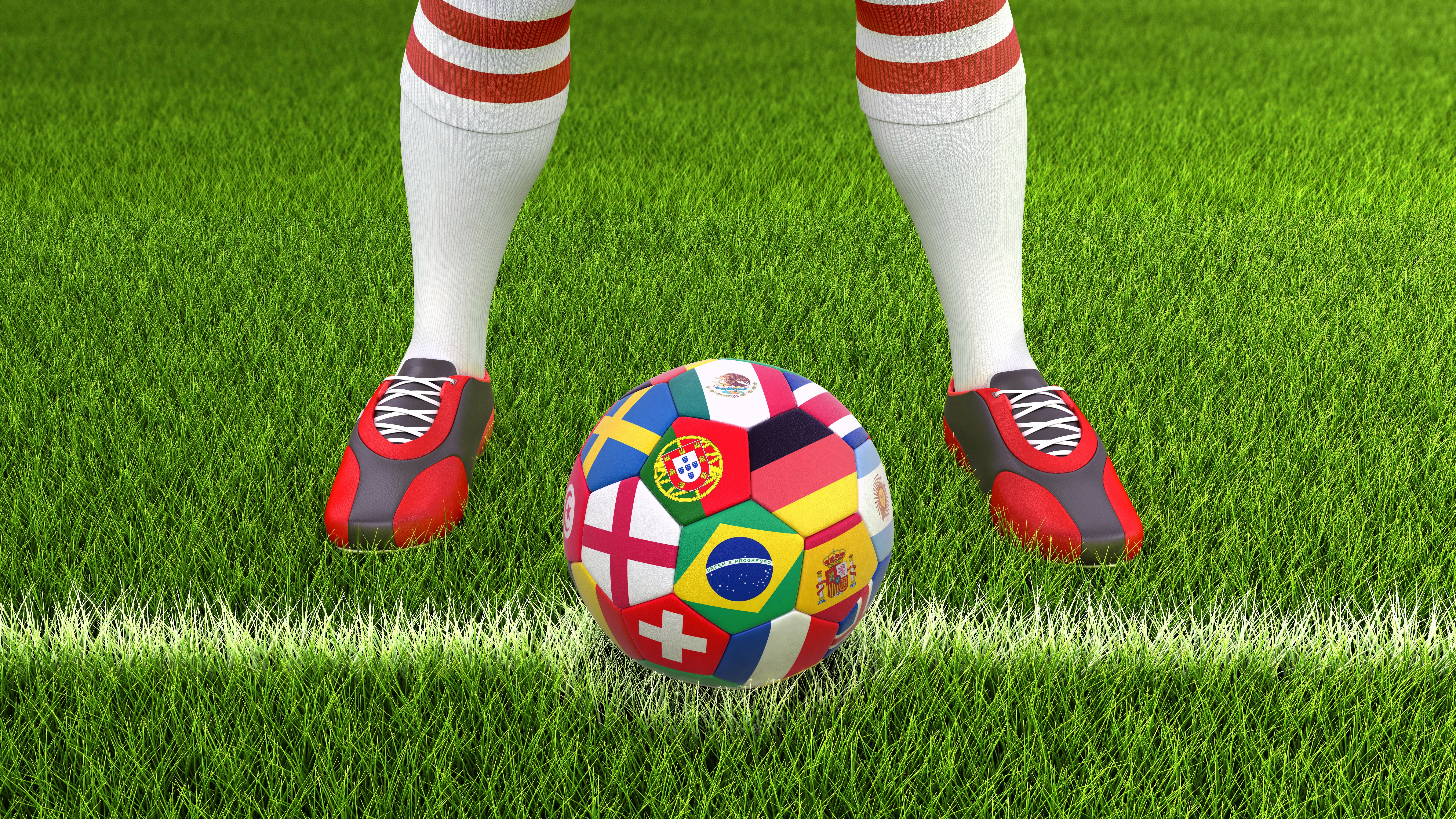 Soccer ball with flags and player legs on grass HD Wallpaper