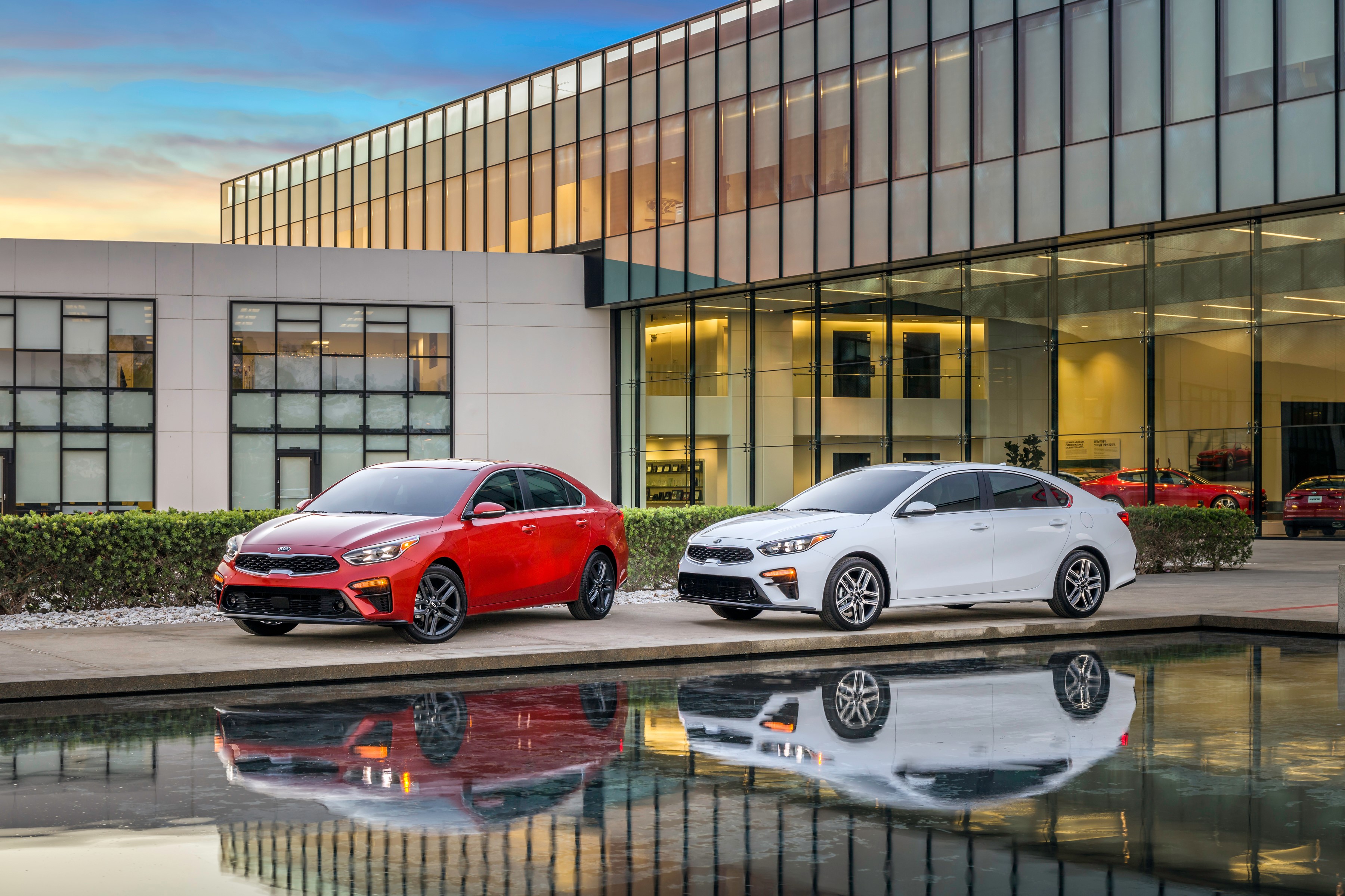 Two Kia Forte cars parked outside a modern building HD Wallpaper