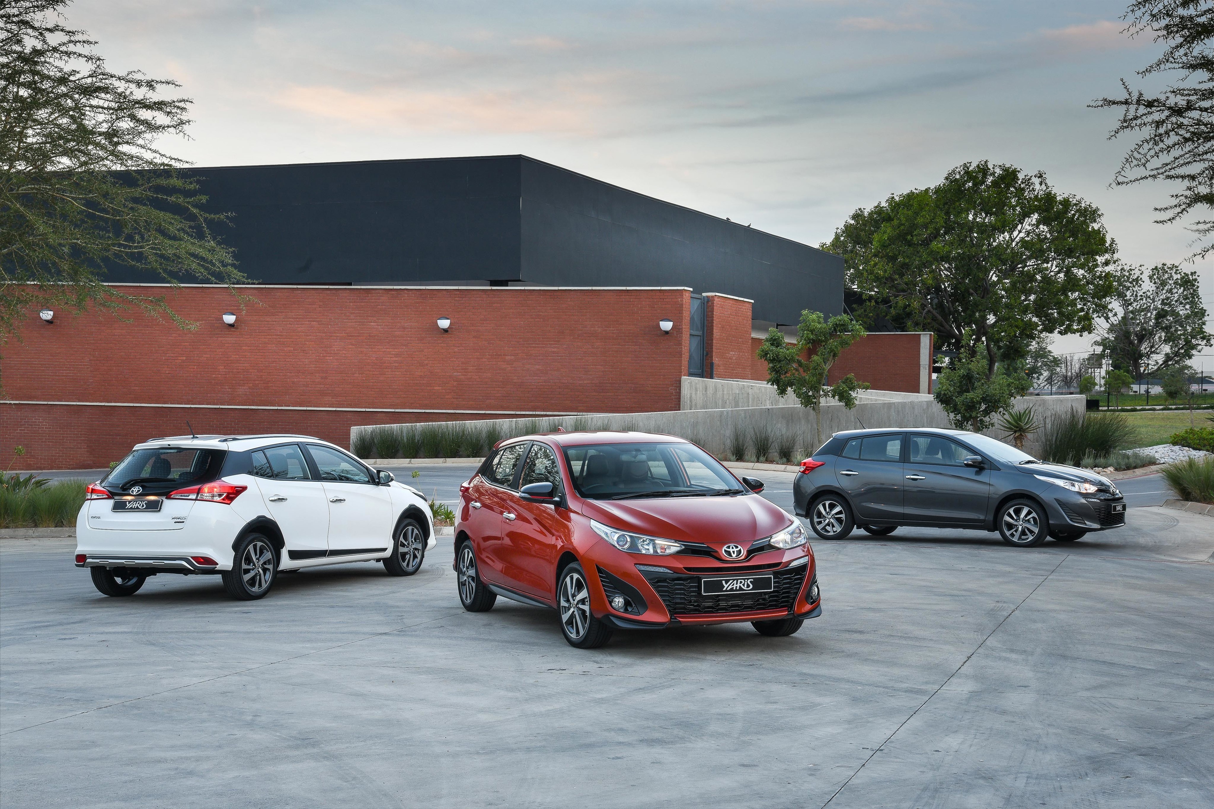 Three Toyota Yaris cars parked outside a modern building HD Wallpaper