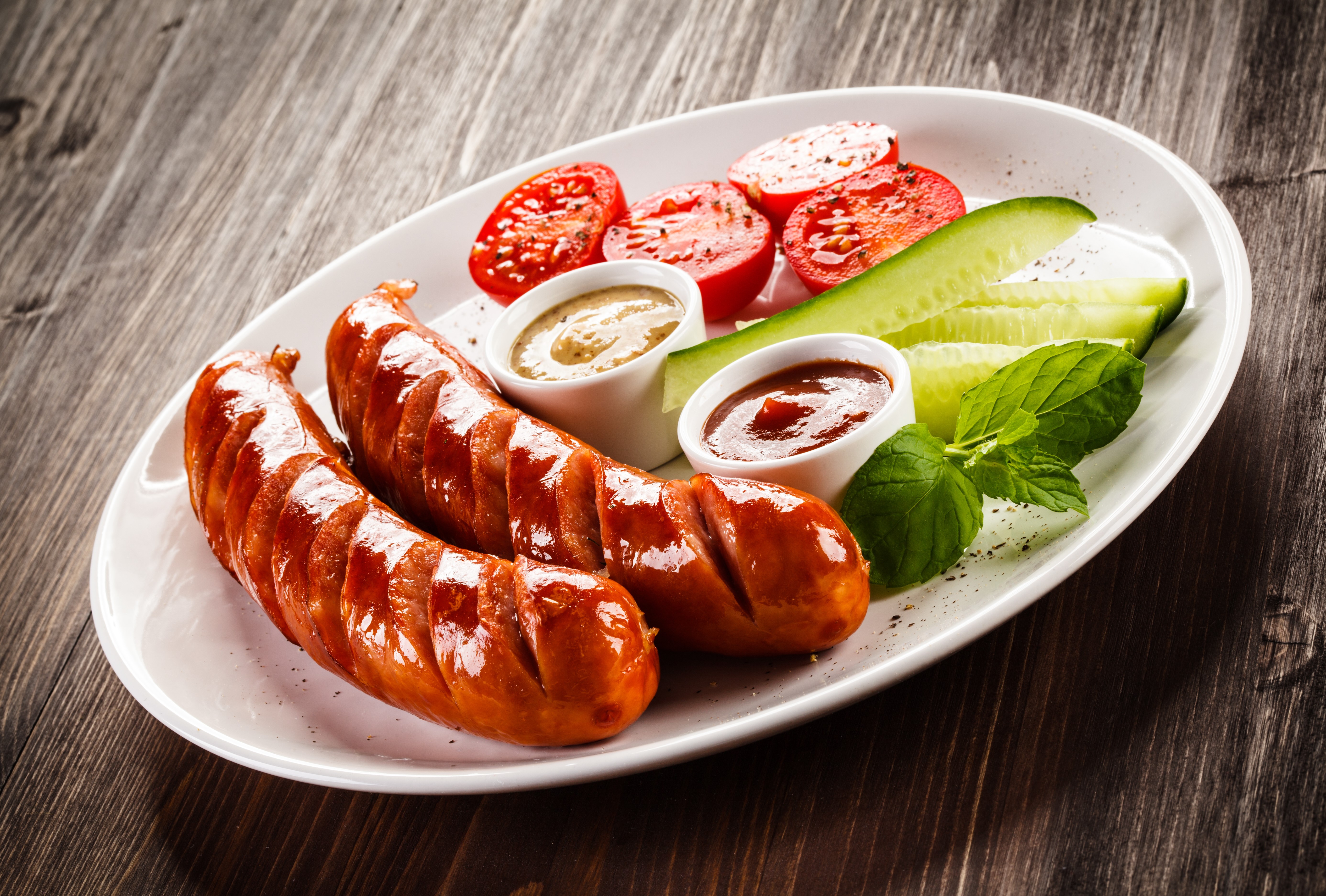 Grilled sausages with tomatoes, cucumbers, and dips on a plate HD Wallpaper