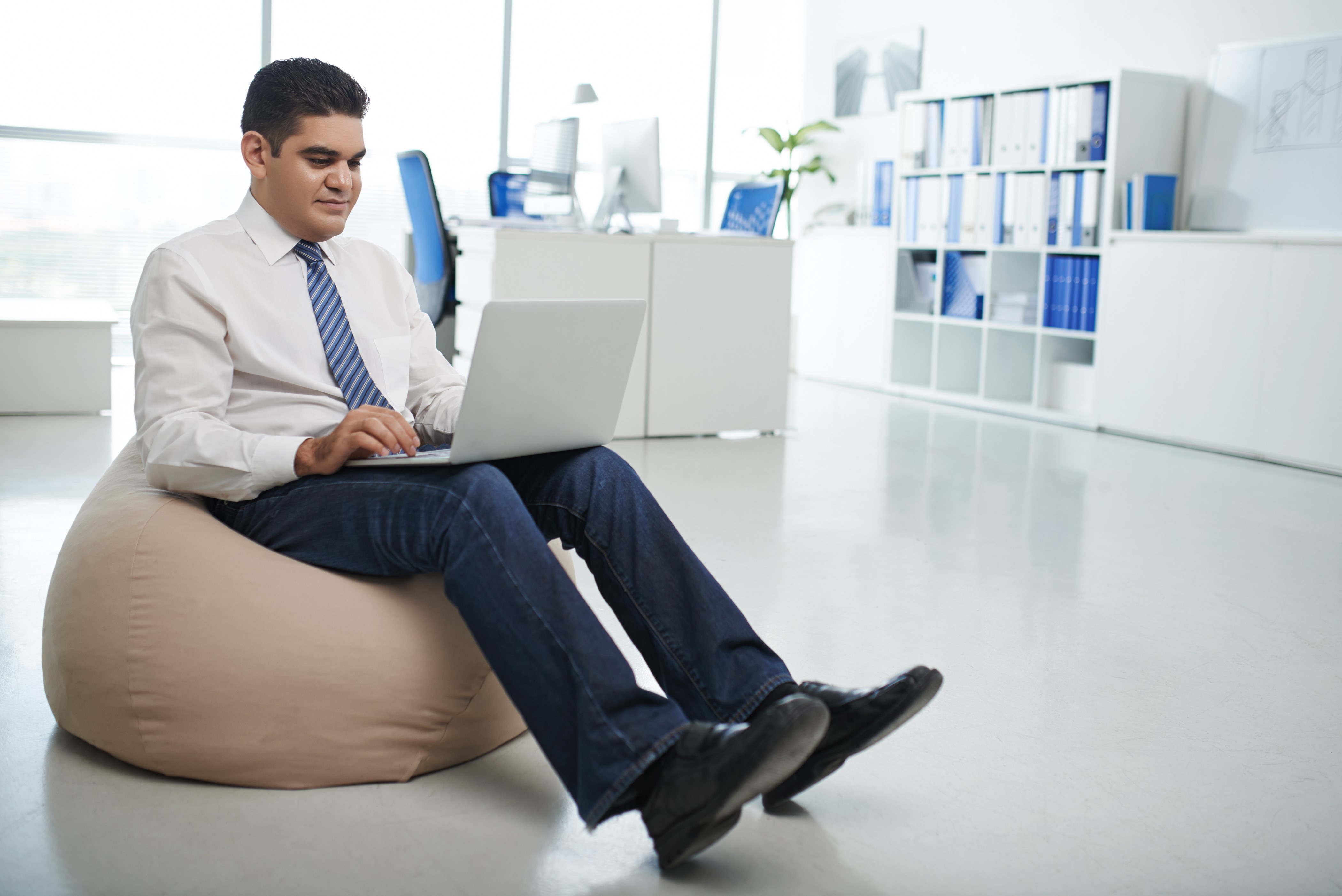 Man in Jeans and Tie Using Laptop on Beanbag HD Wallpaper