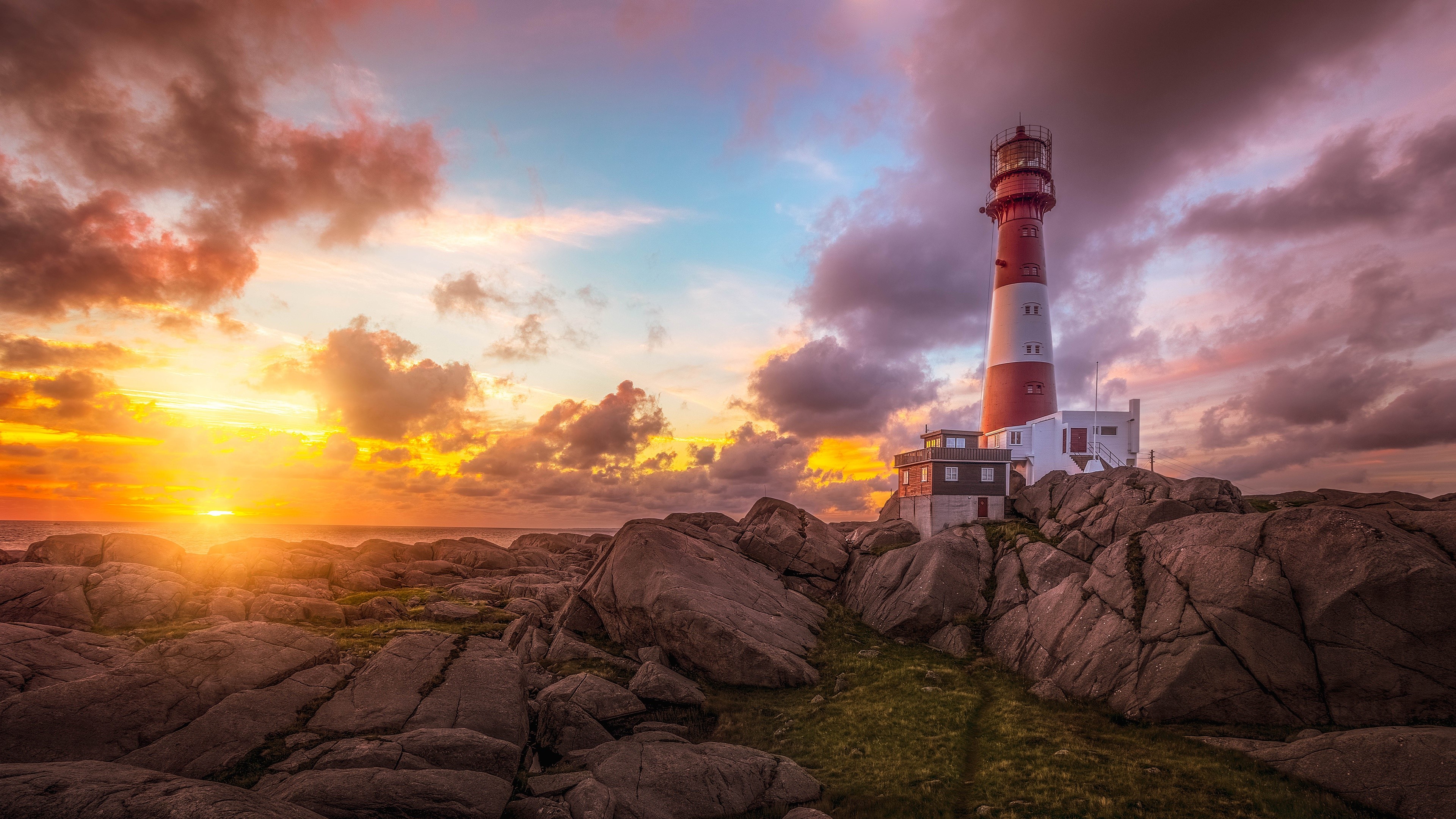 Lighthouse on rocky shore at sunset HD Wallpaper