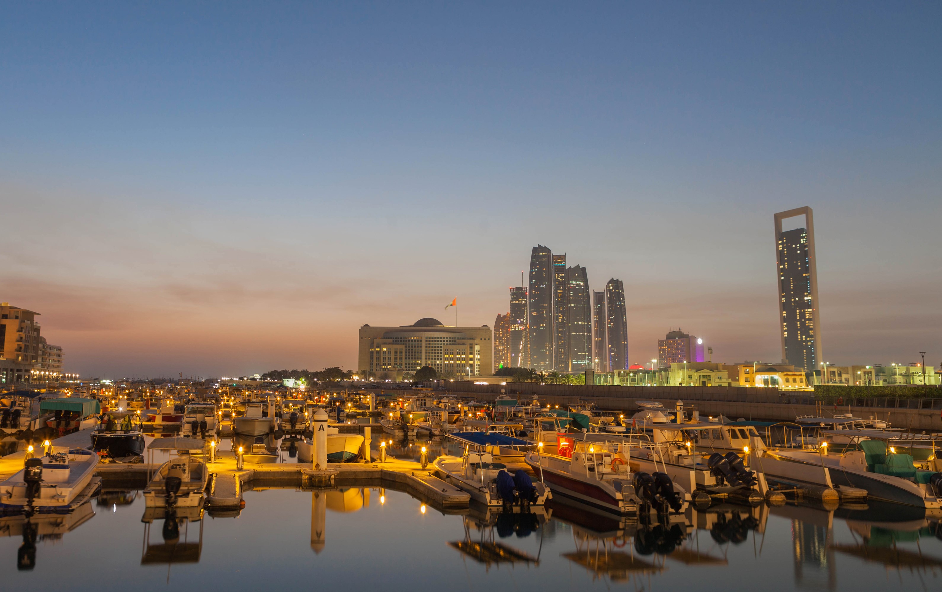 Boats docked in a marina with city skyline at dusk HD Wallpaper