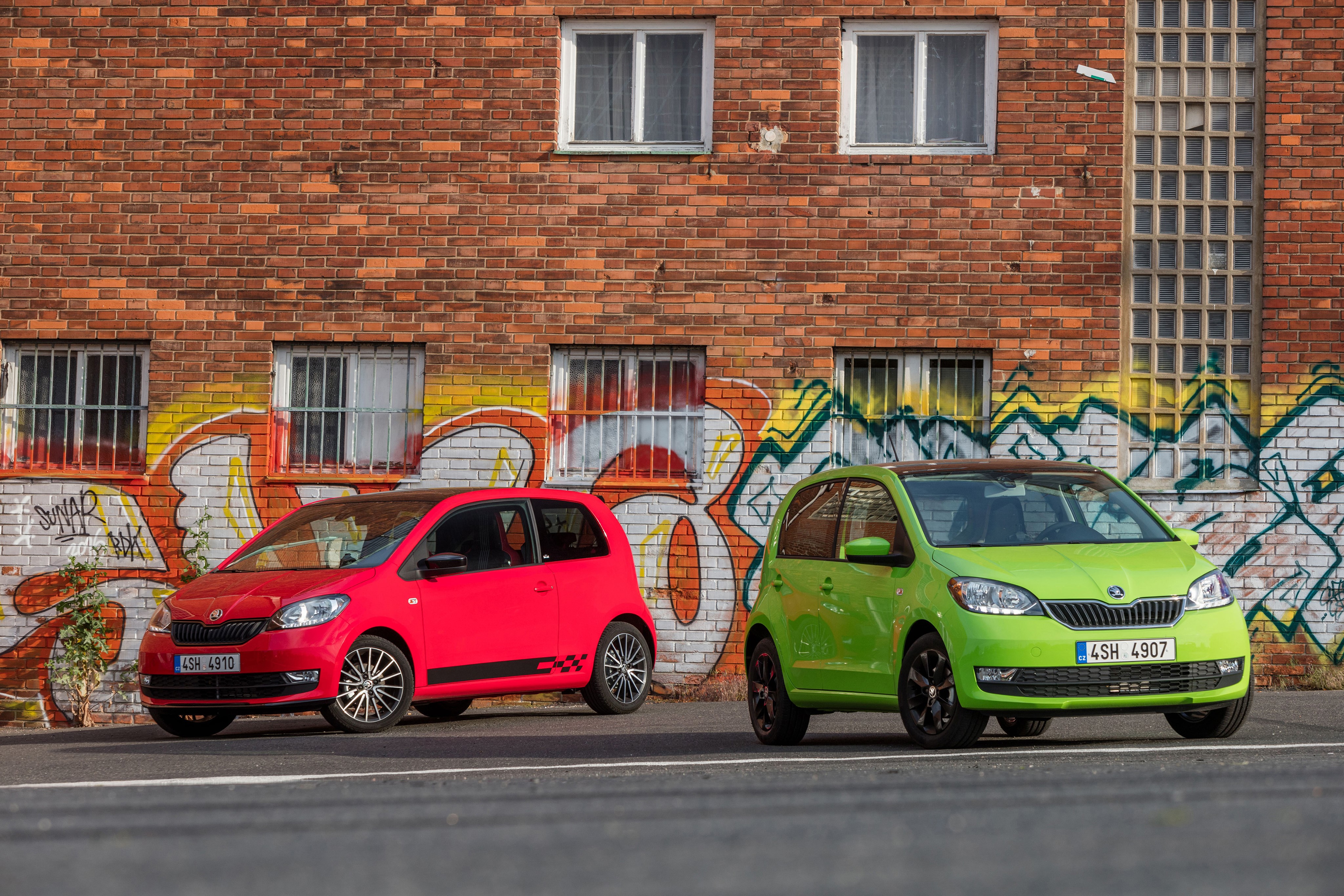Two Skoda Citigo cars in front of a brick wall with graffiti HD Wallpaper