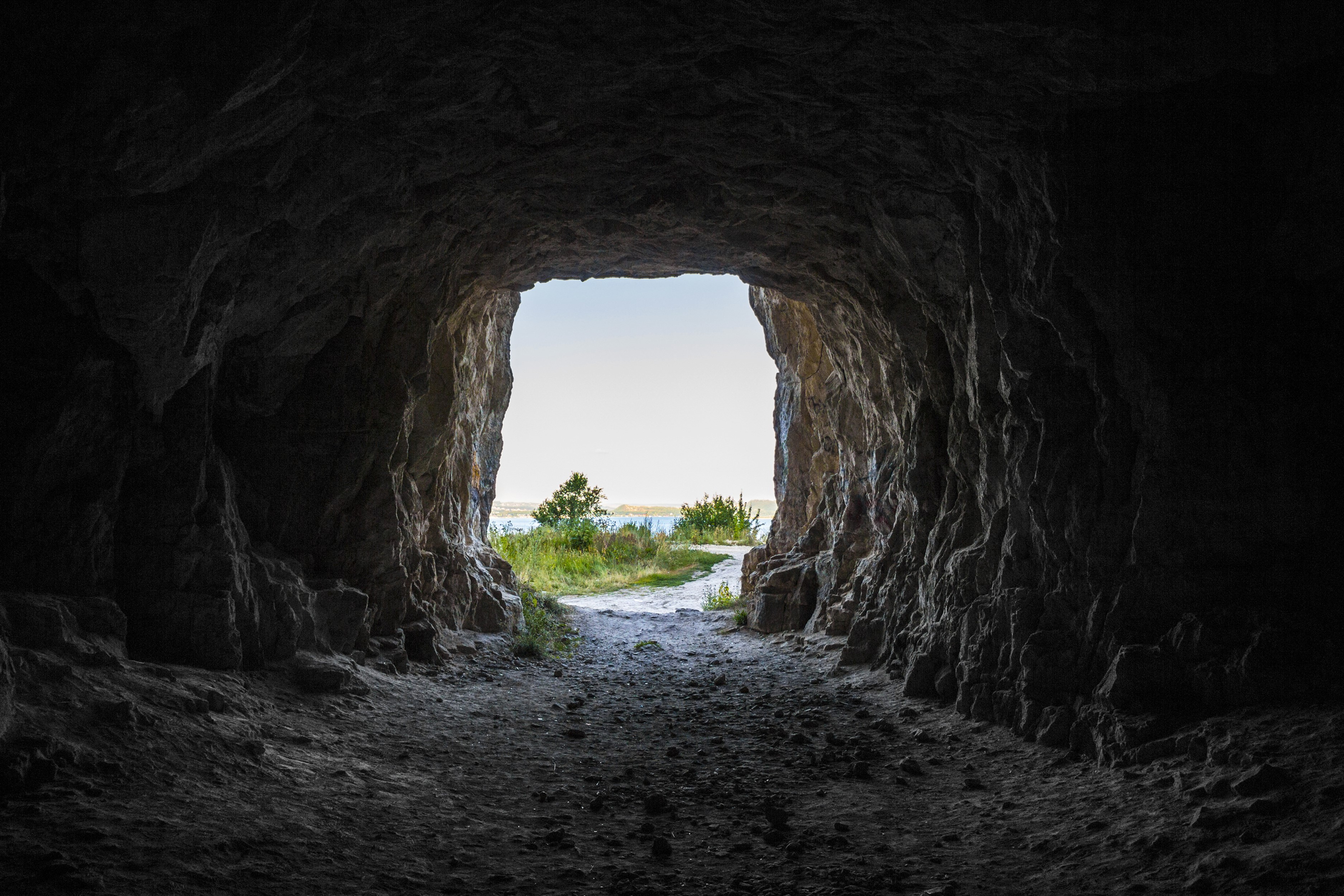 View from inside a dark cave looking out to a bright landscape HD Wallpaper