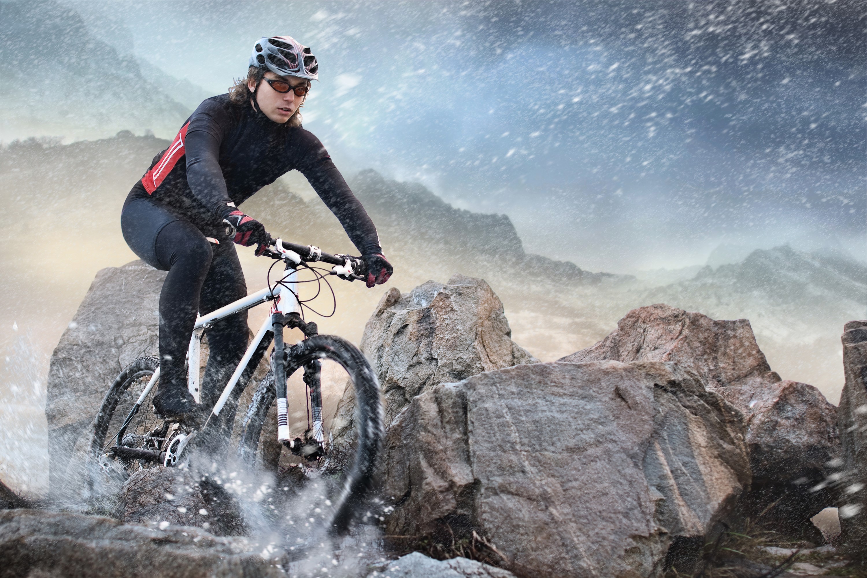 Mountain biker riding through rocks and snow HD Wallpaper