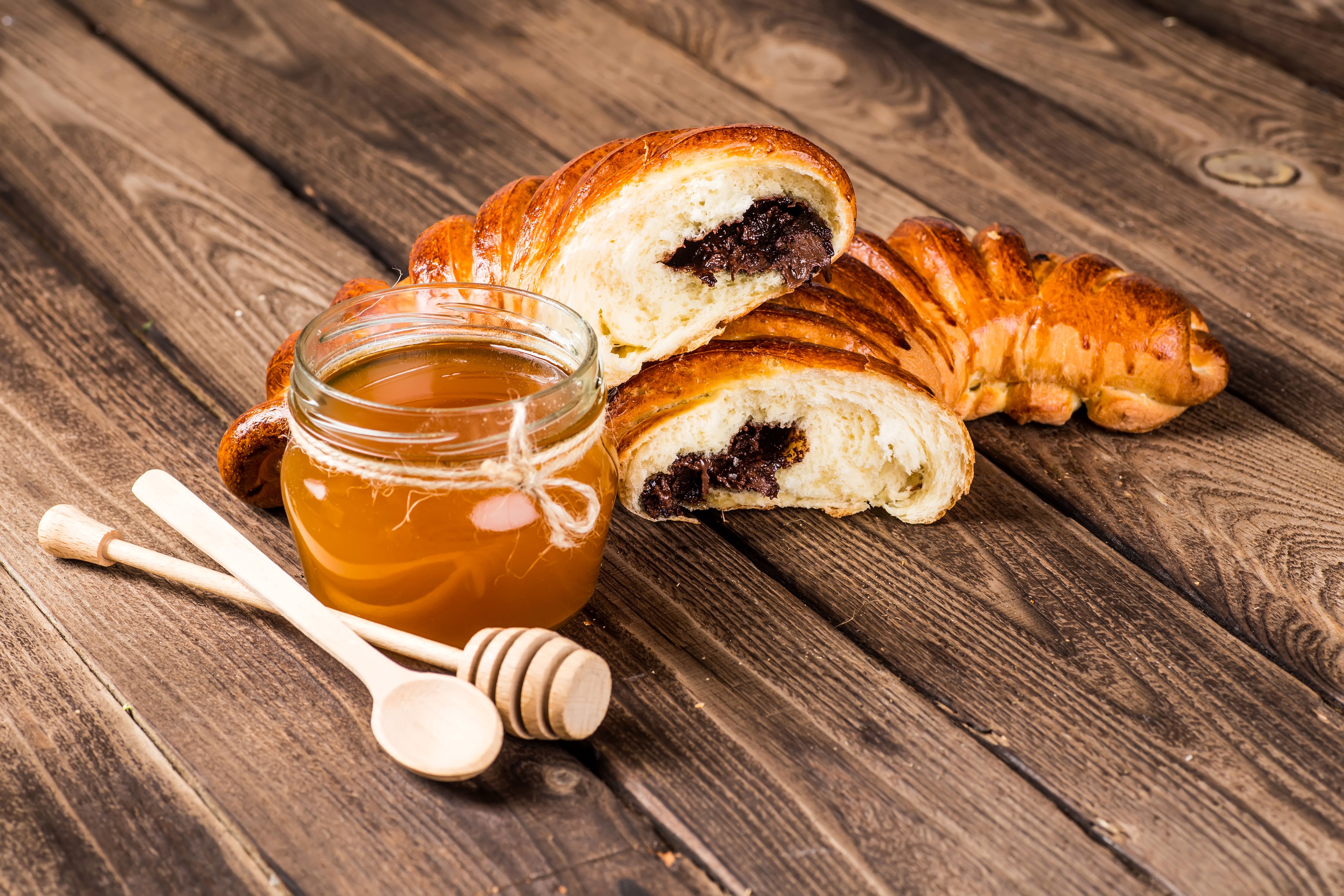 Honey in a jar with croissants and honey dippers on wood planks HD Wallpaper