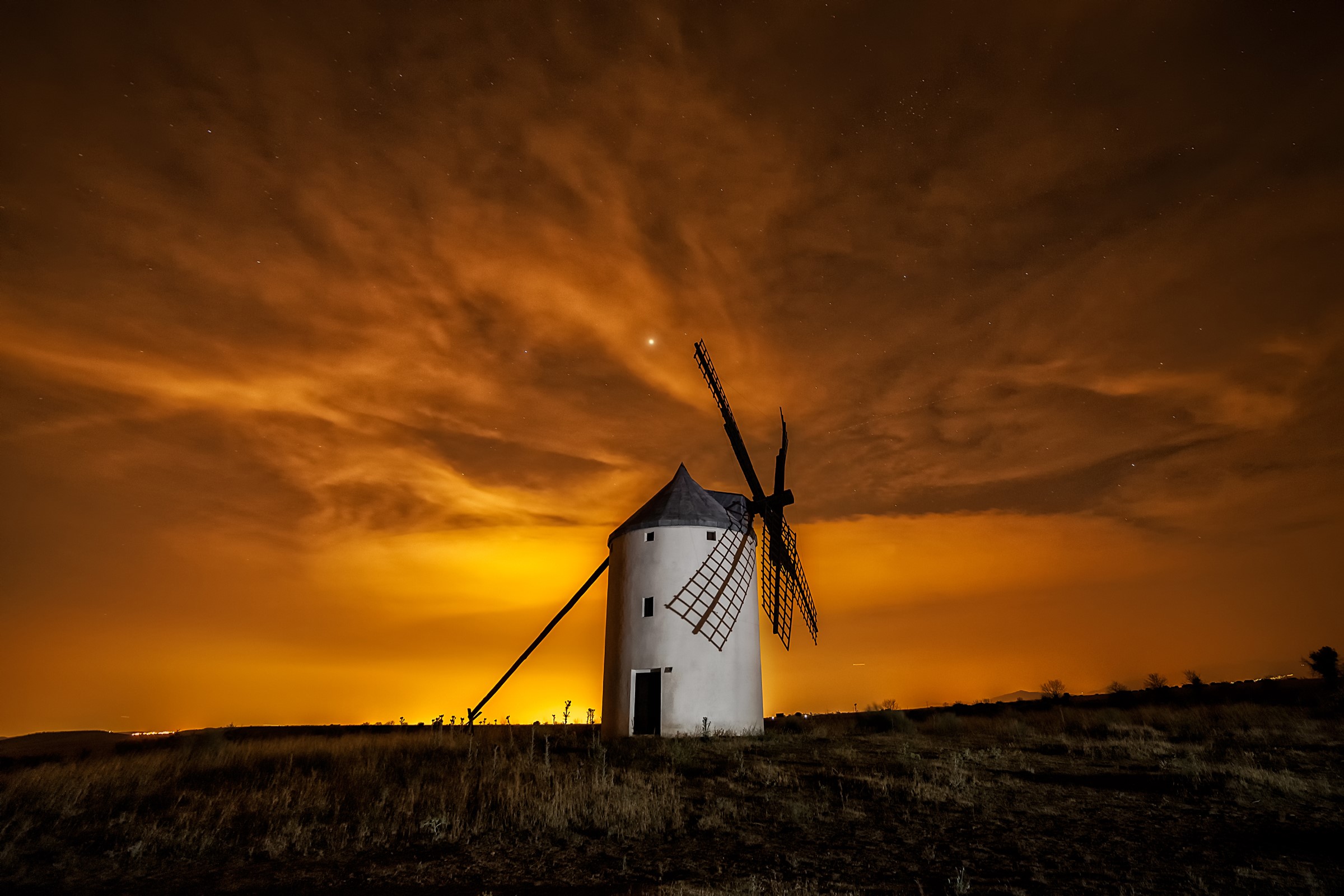 Windmill under a dramatic orange sky at night HD Wallpaper