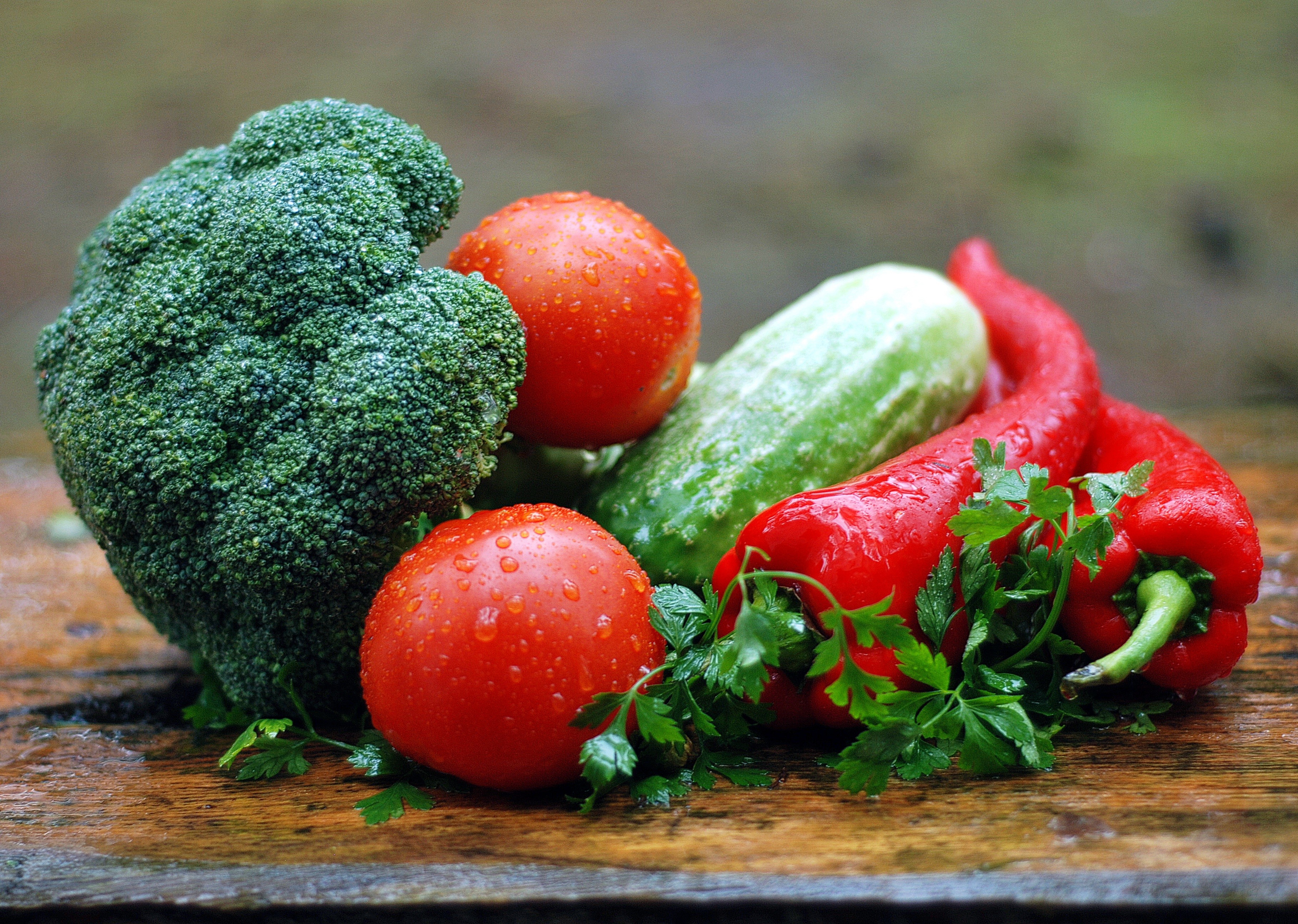 Broccoli, tomatoes, cucumber, bell peppers, and parsley on a wooden surface HD Wallpaper