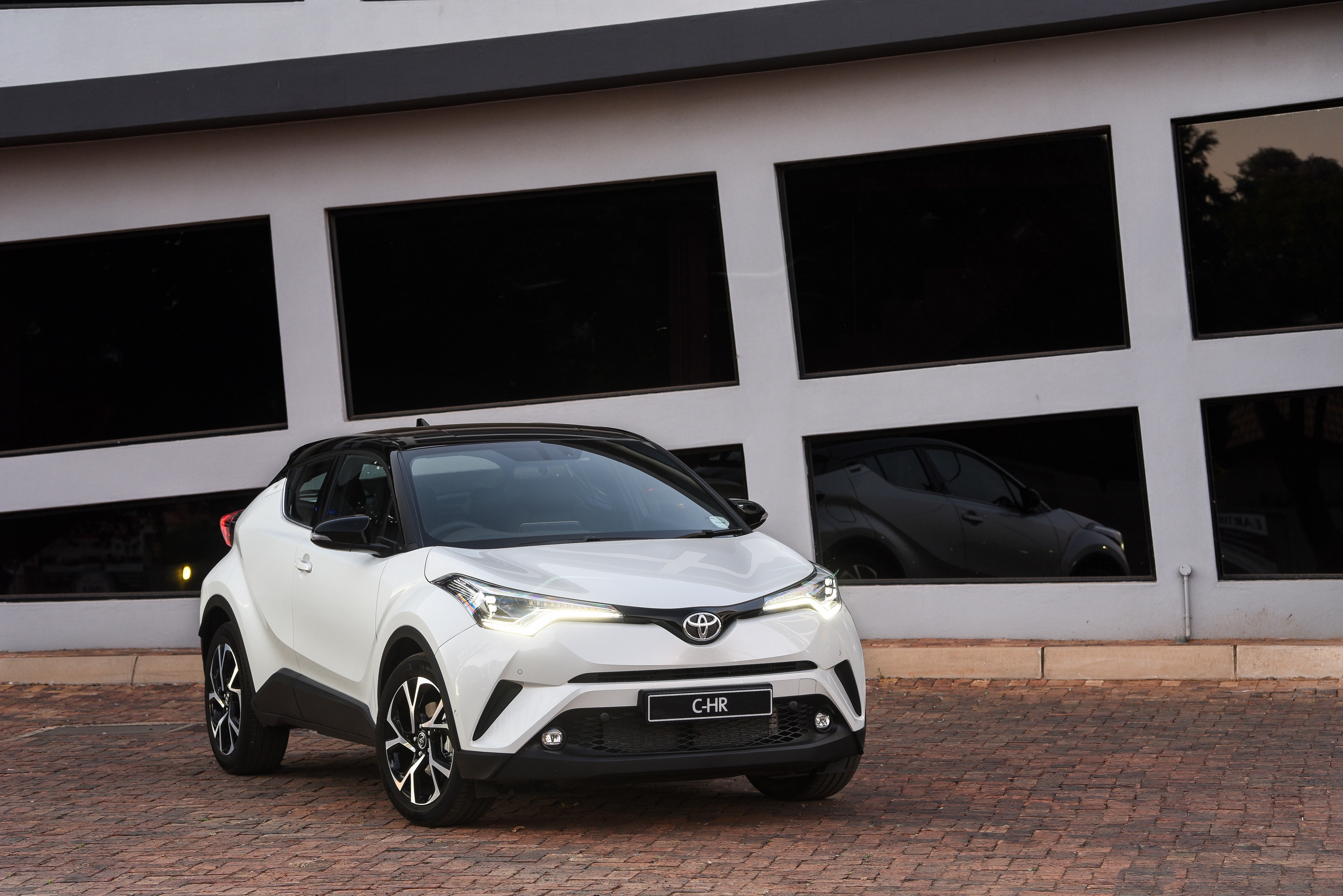 White Toyota C-HR parked in front of a modern building HD Wallpaper