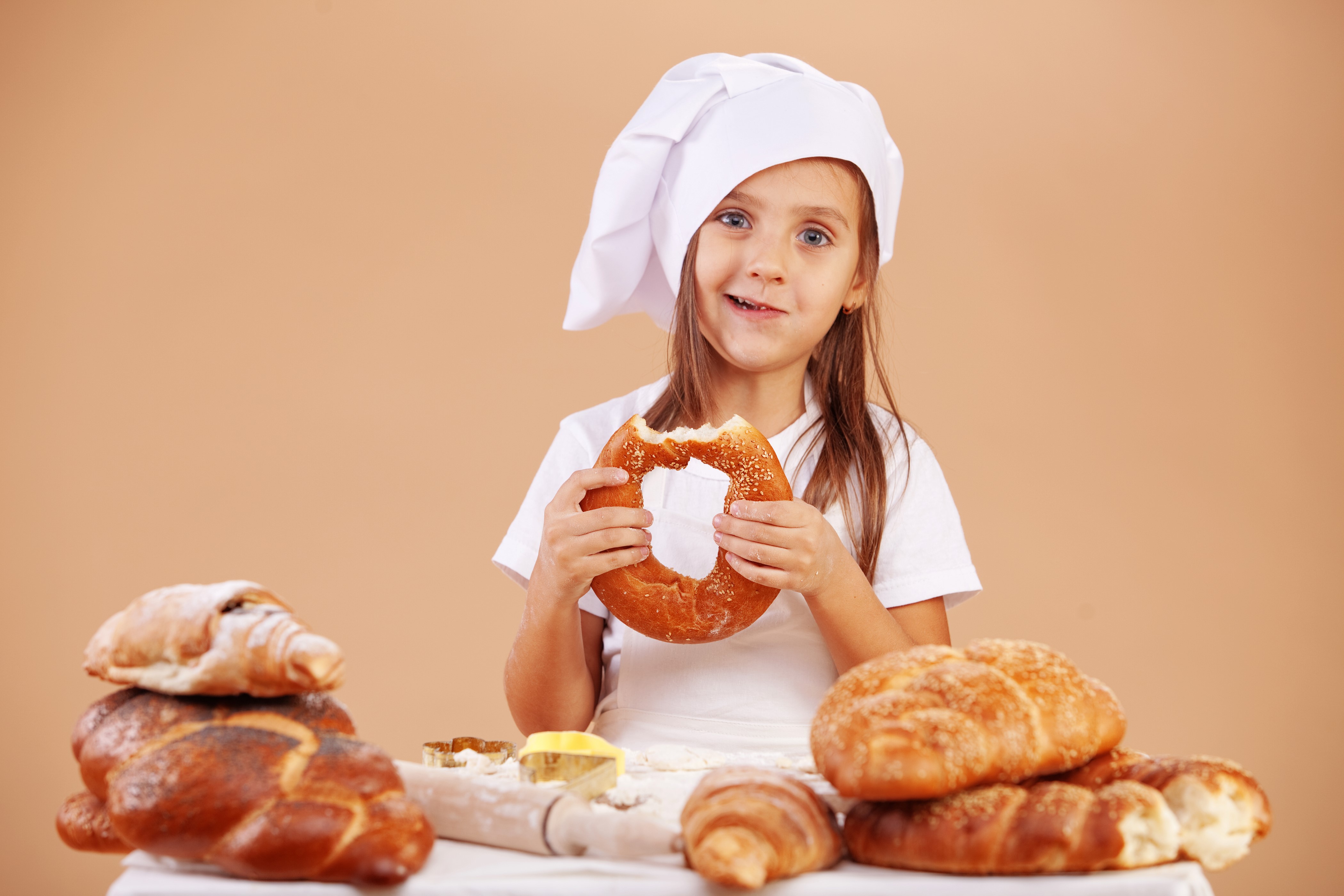 Little girl in chef hat eating bagel with pastries HD Wallpaper