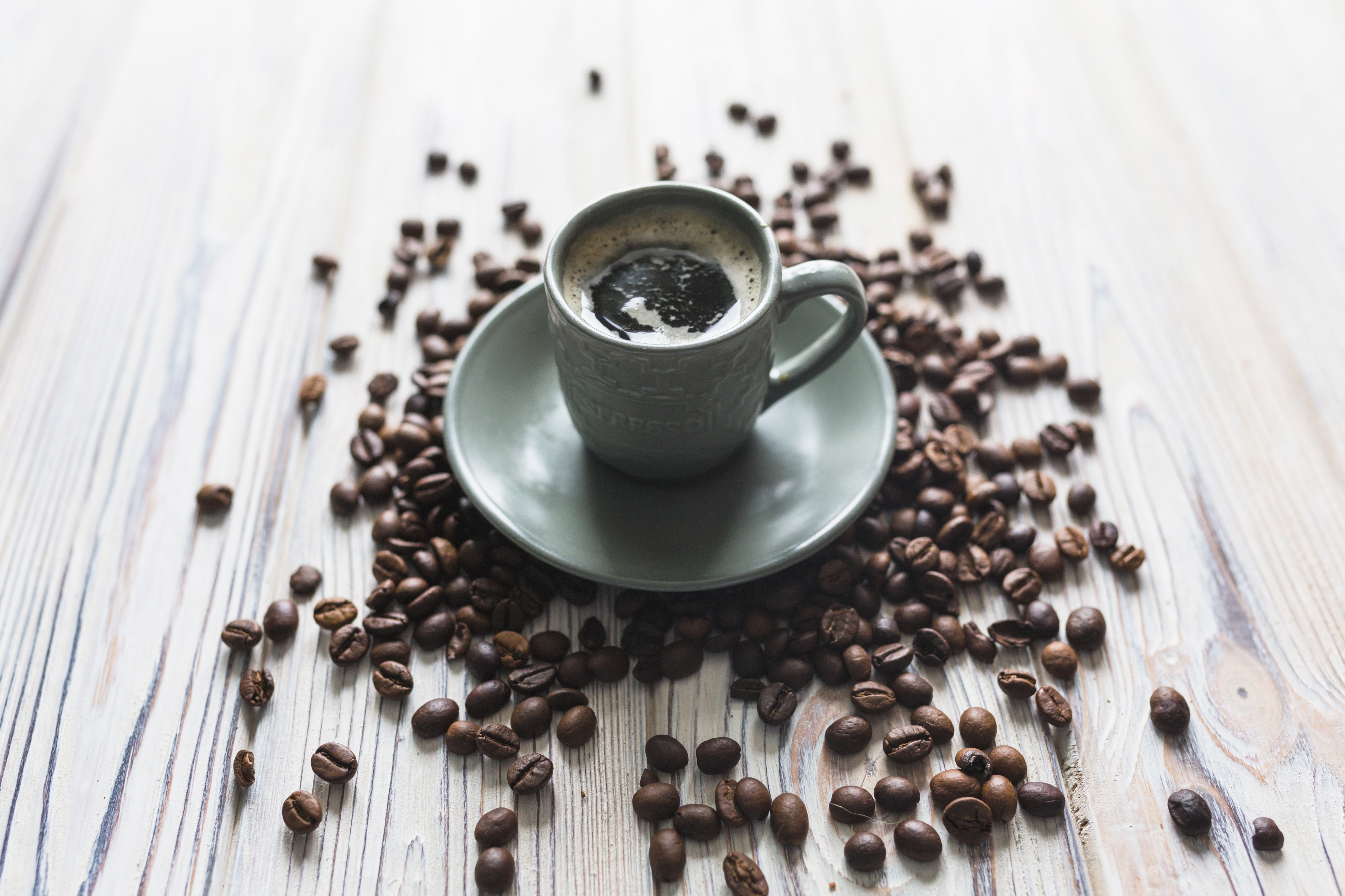 Coffee cup and saucer surrounded by coffee beans HD Wallpaper