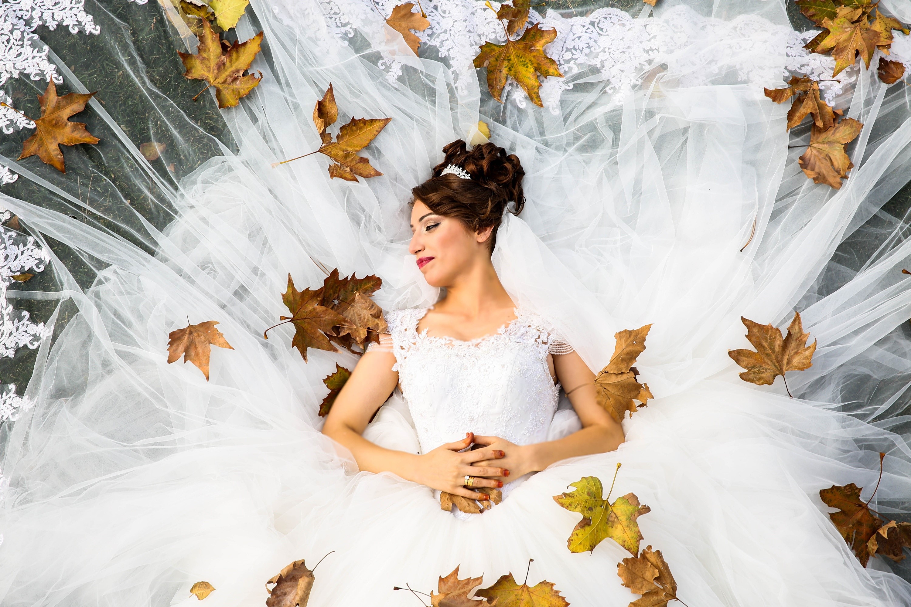 Bride in wedding dress lying among autumn leaves HD Wallpaper