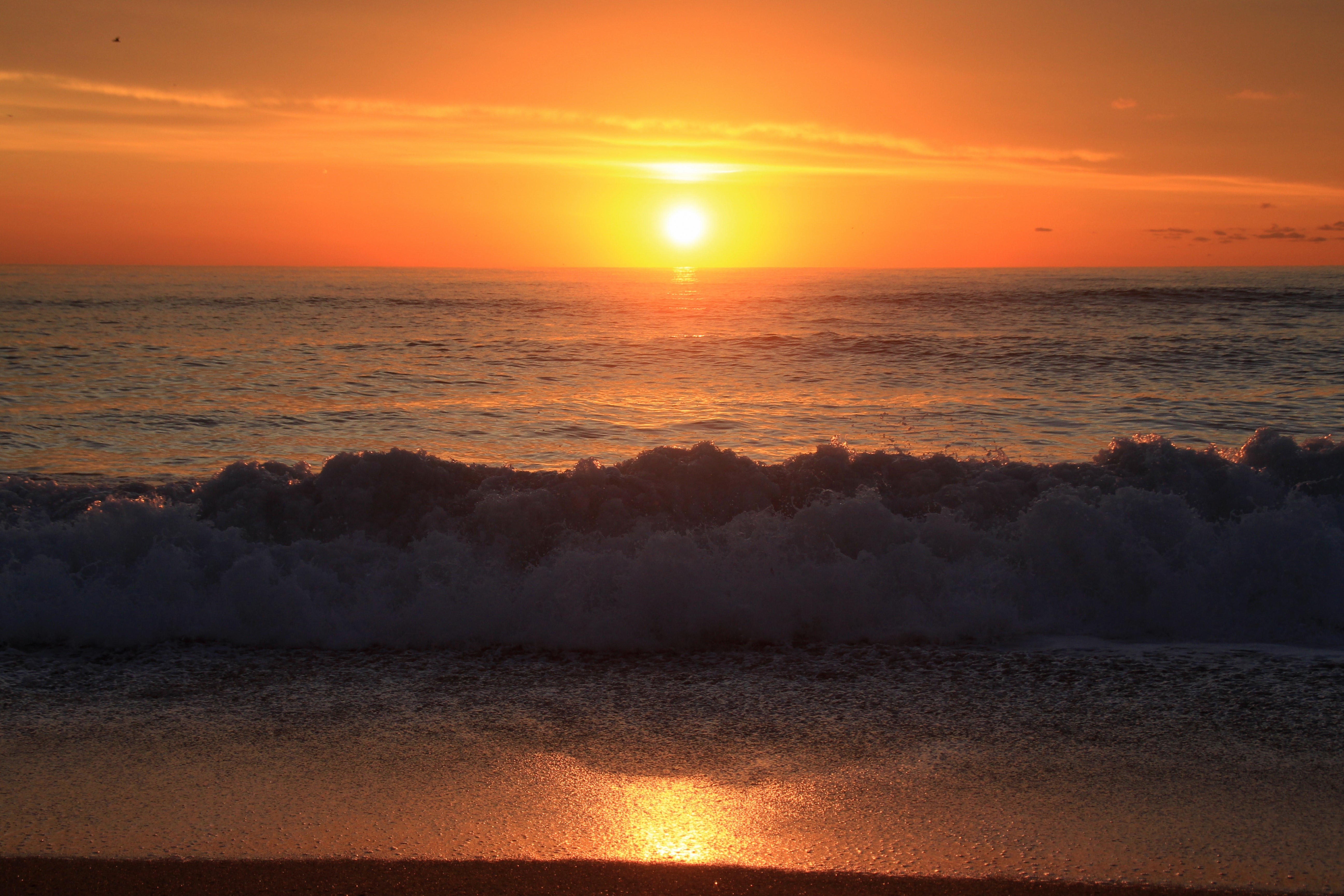 Sunset over the ocean with waves crashing on the beach HD Wallpaper