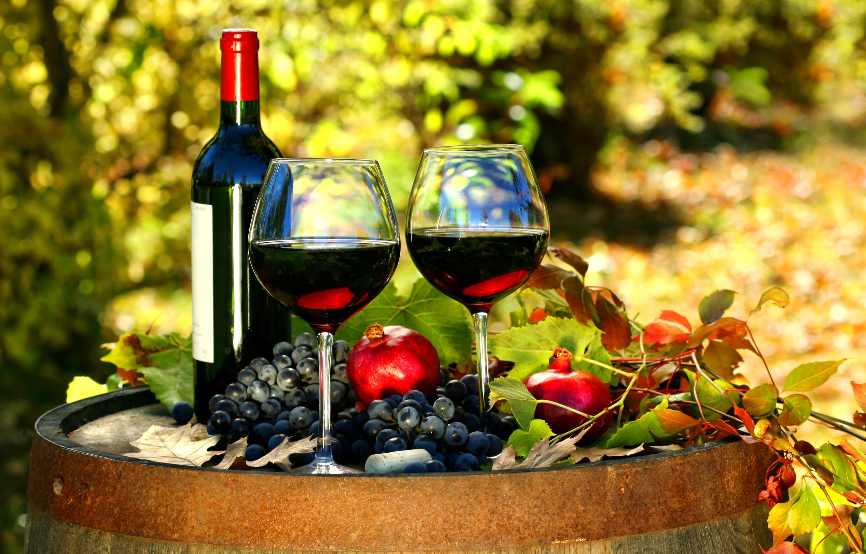 Bottle of wine with two glasses, grapes, and pomegranates on a barrel HD Wallpaper