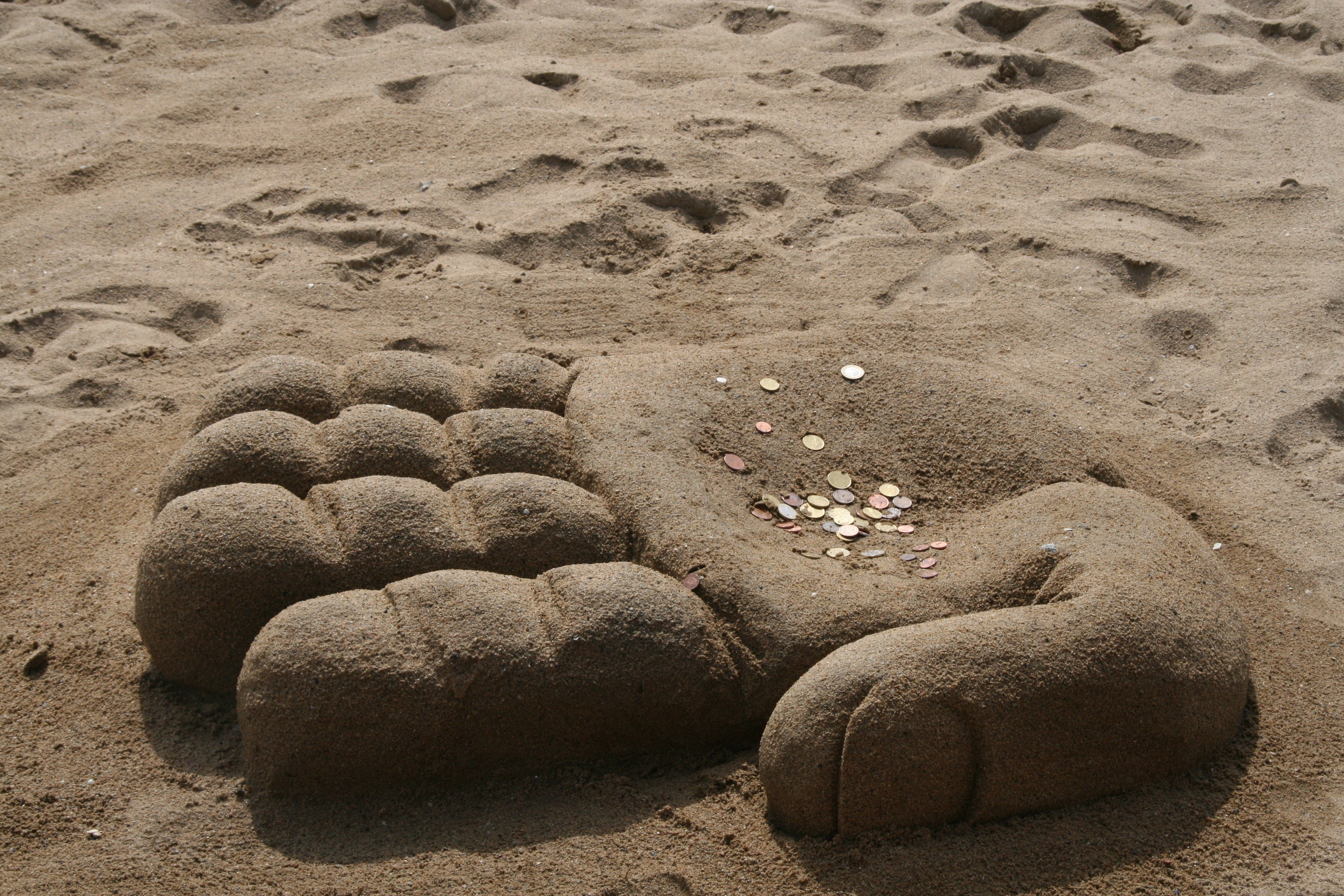 Sand sculpture of a hand with coins HD Wallpaper