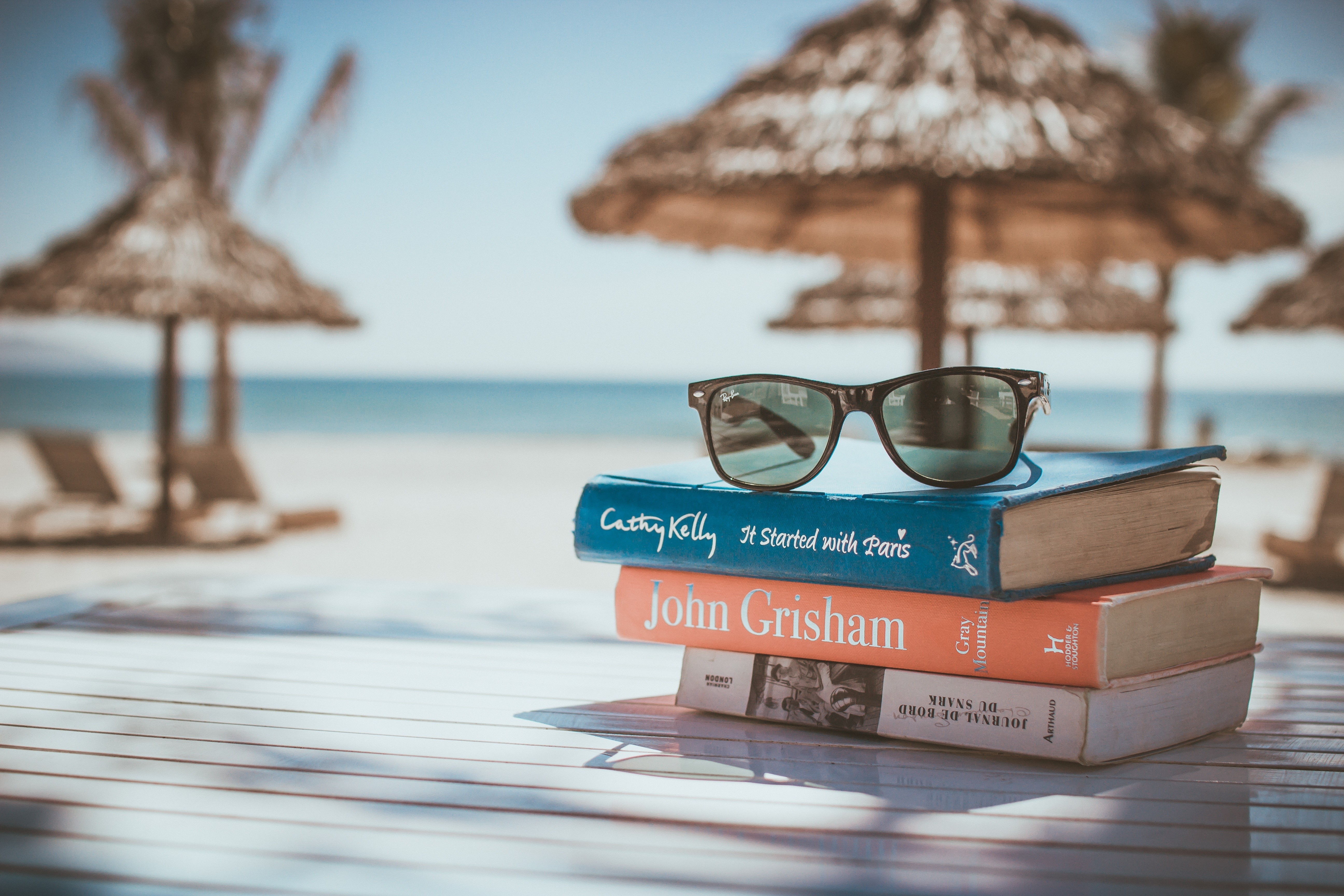 Stack of books and sunglasses on a table at the beach HD Wallpaper