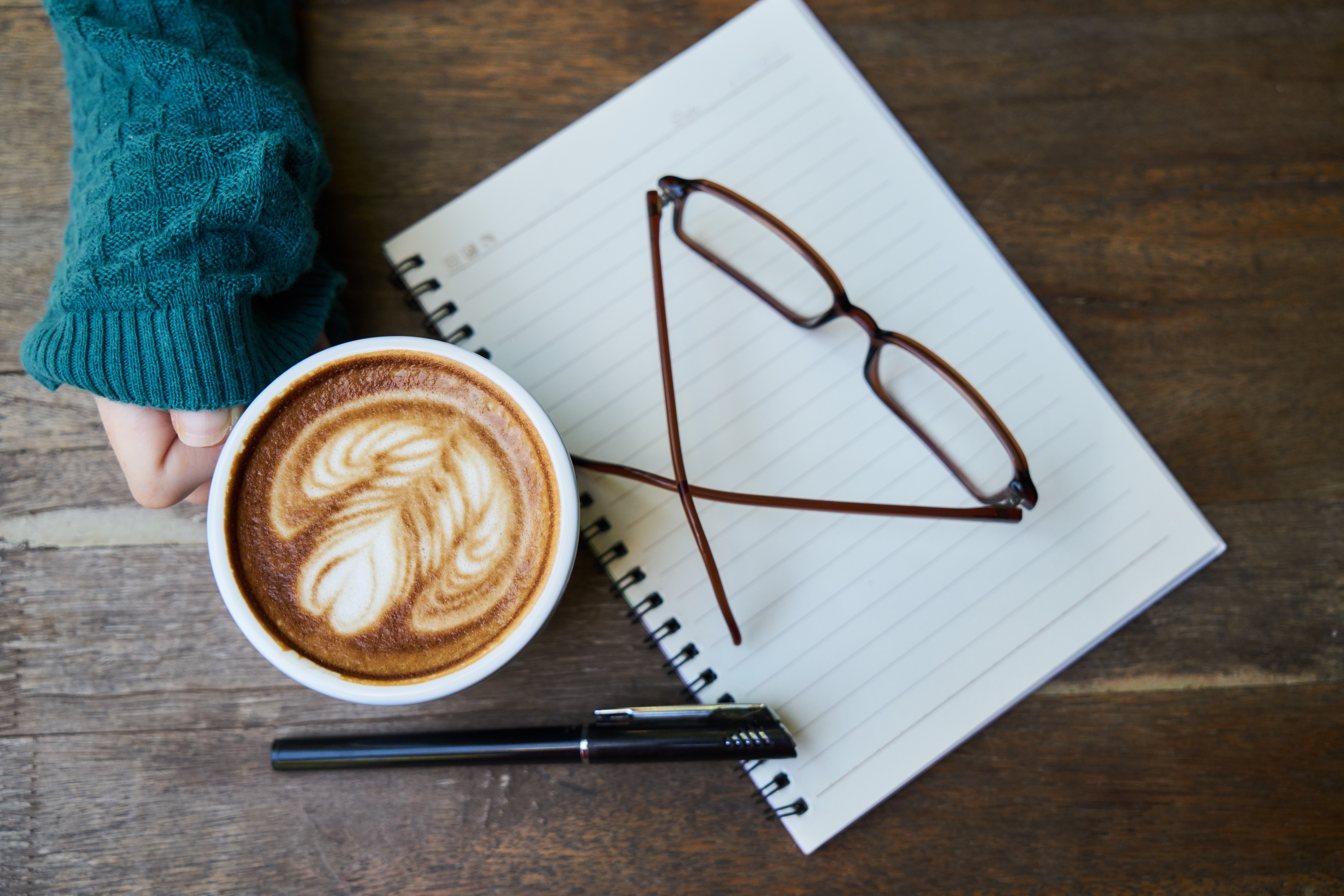 Coffee cup, glasses, pen, and notepad on wooden table HD Wallpaper