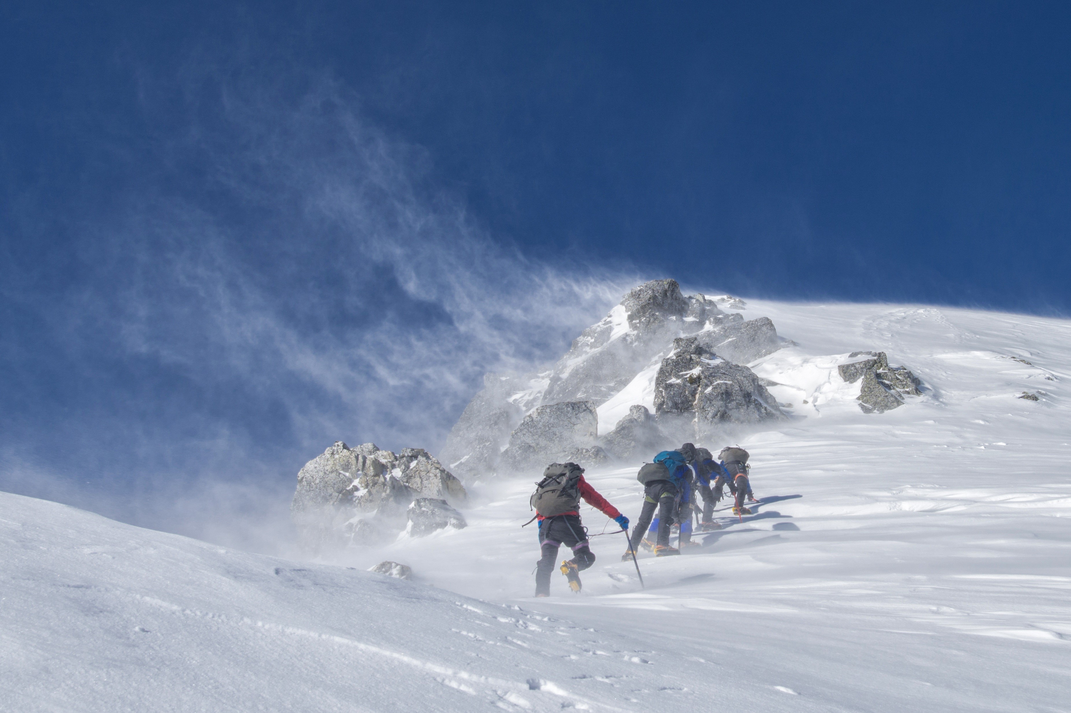 Mountaineers climbing a snowy mountain in strong winds HD Wallpaper