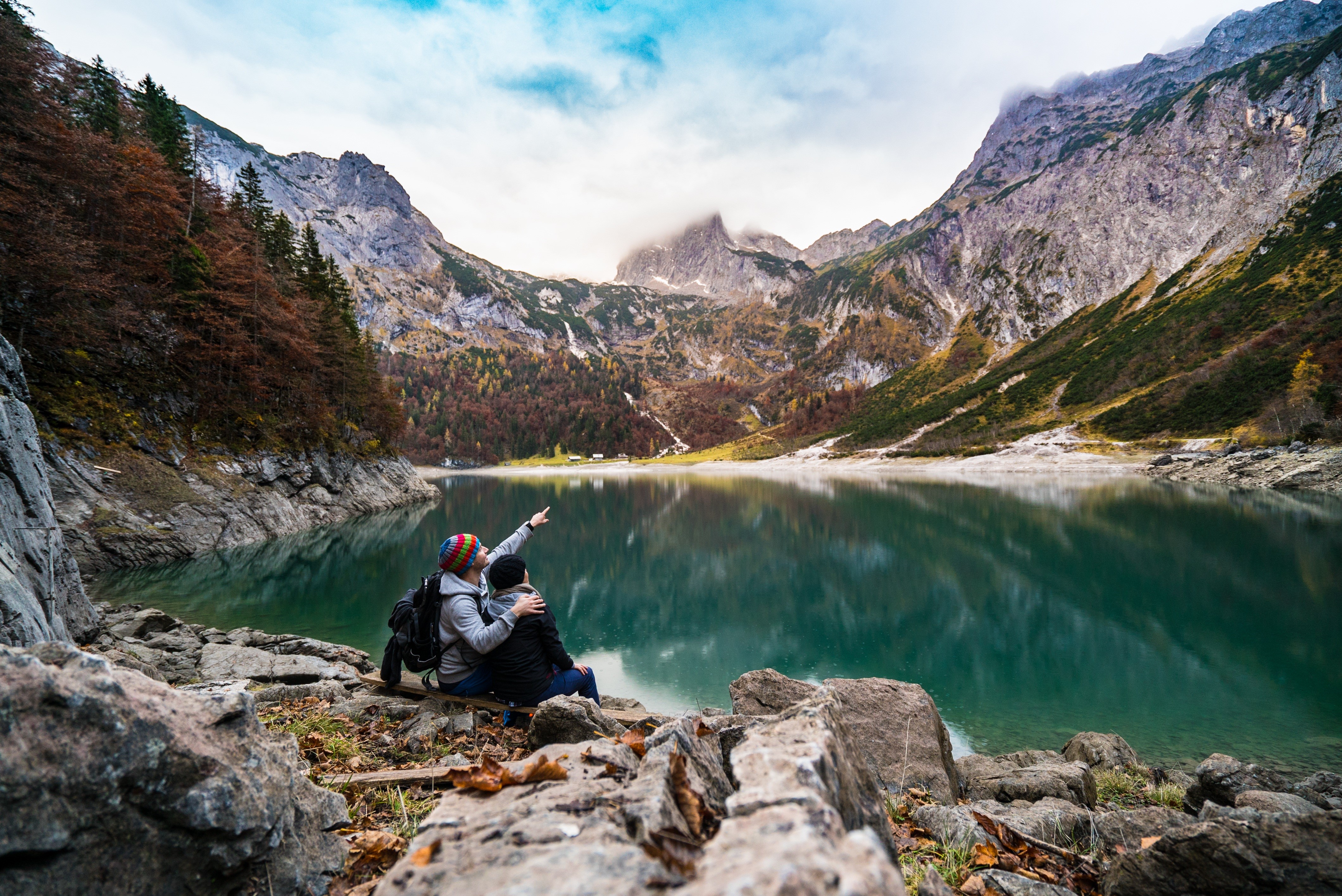 Two people sitting by a lake with mountains HD Wallpaper