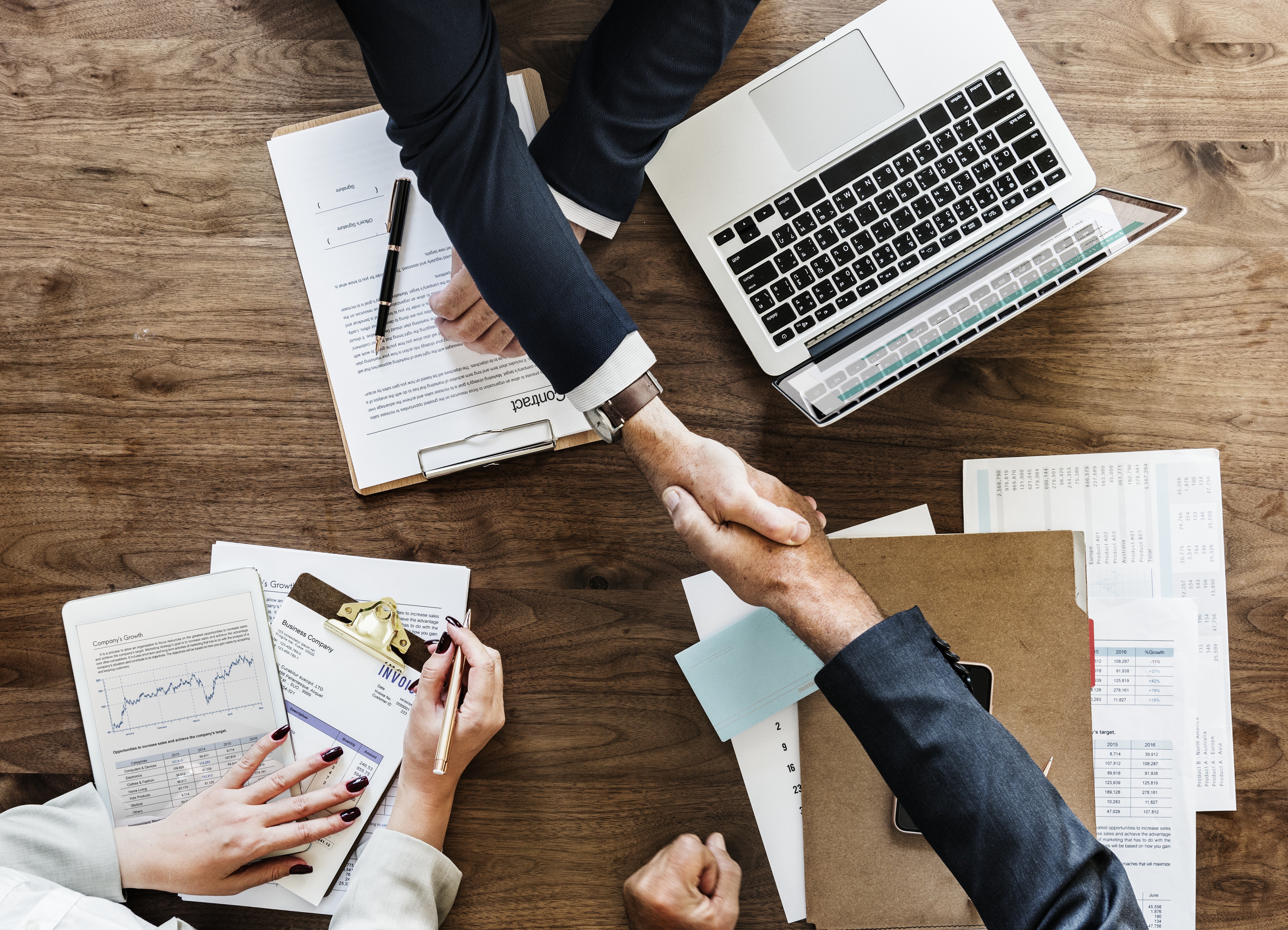 Business people shaking hands over a contract with laptop and tablet HD Wallpaper