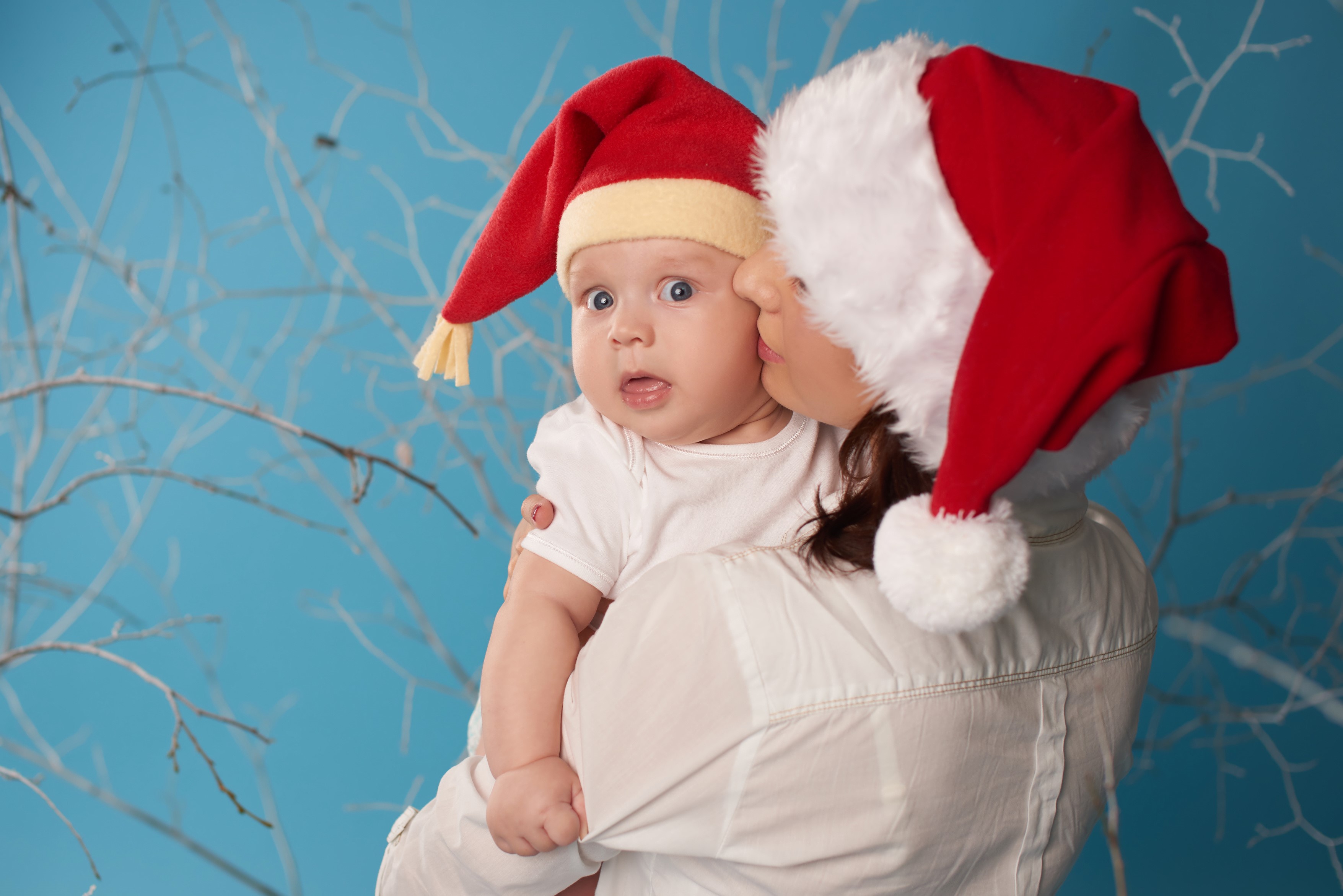 Mother kissing baby wearing Santa hats HD Wallpaper