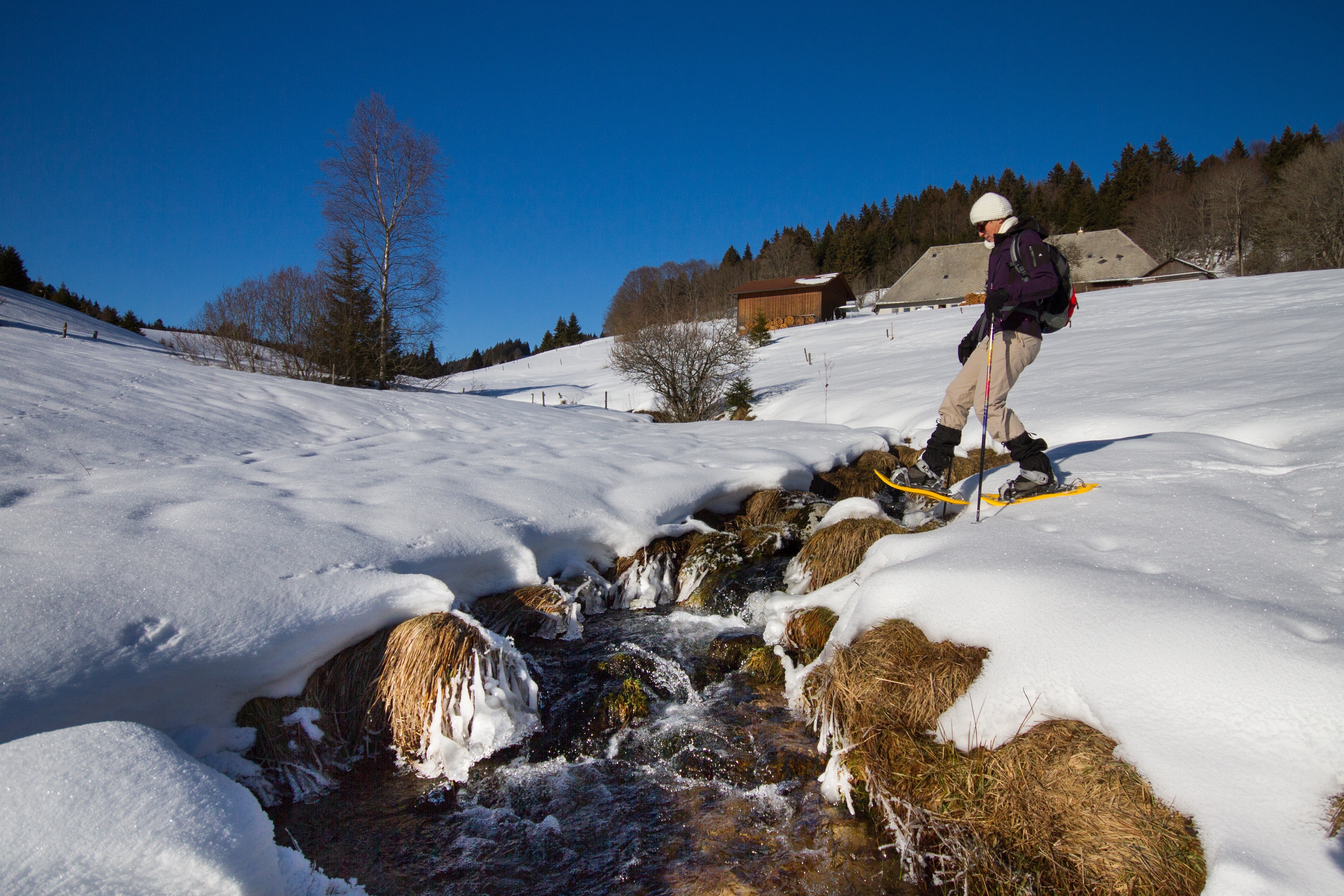 Person snowshoeing across a stream in winter HD Wallpaper