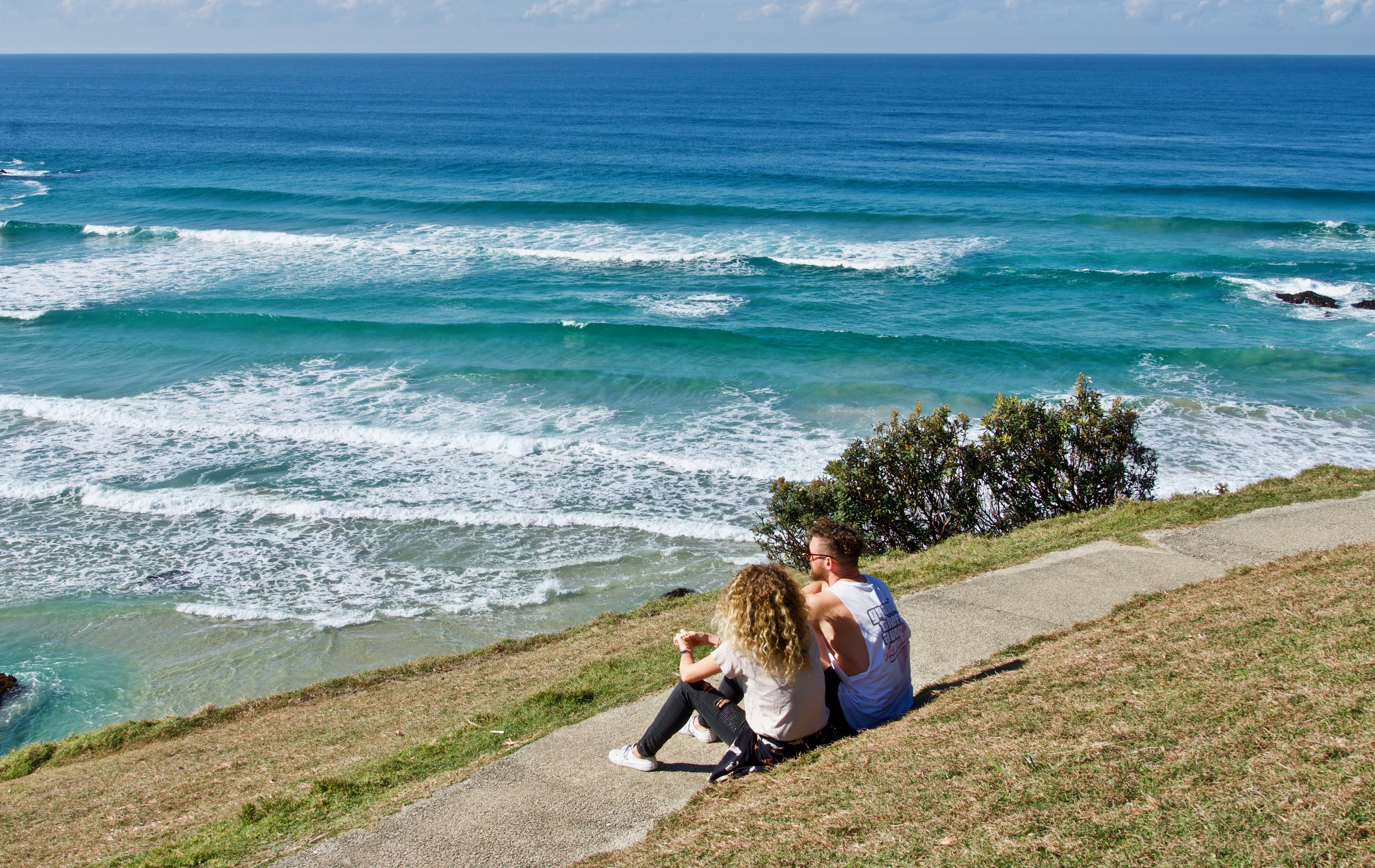Couple Sitting on a Grassy Hill Overlooking the Ocean HD Wallpaper