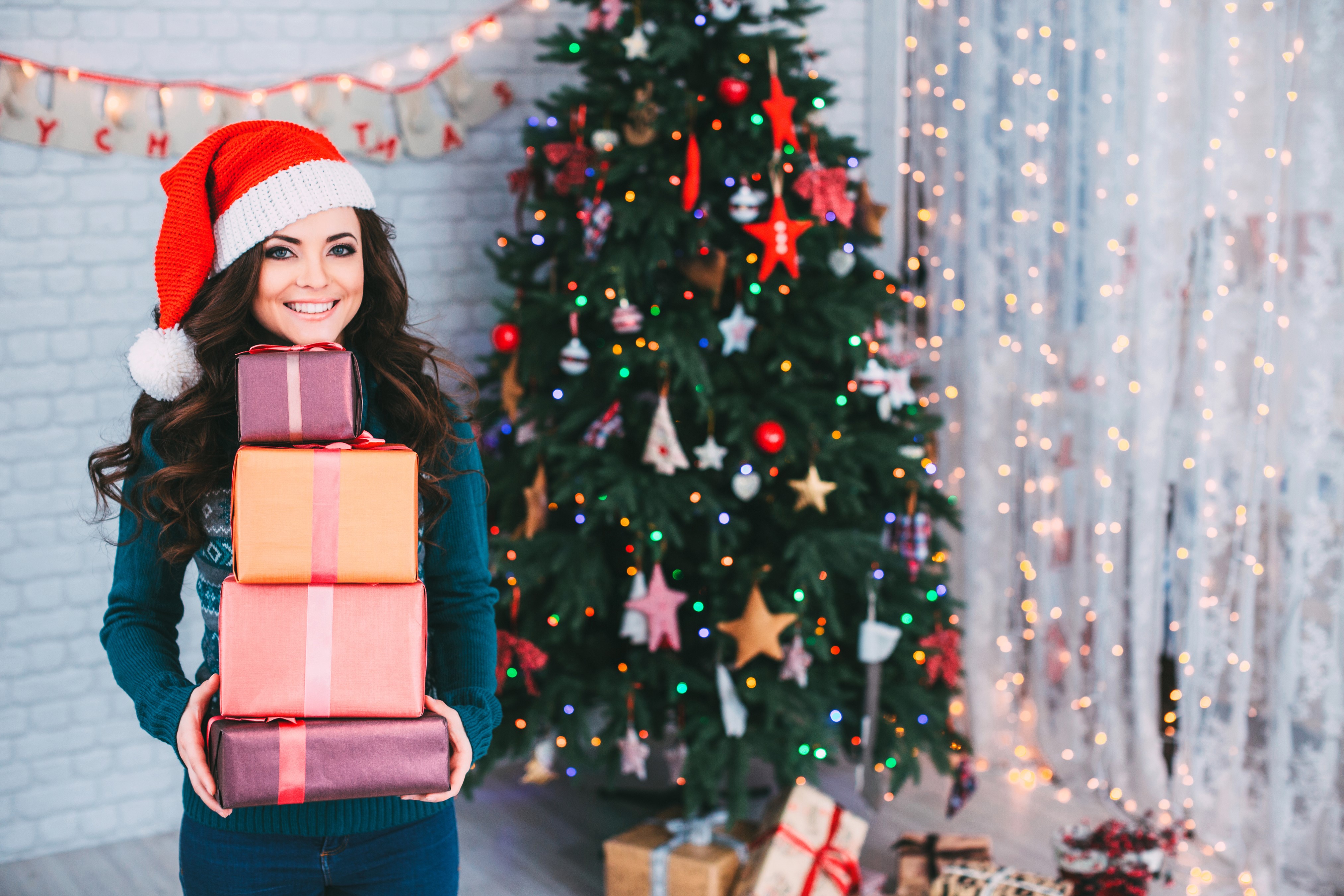 Brunette girl in Santa hat holding Christmas gifts HD Wallpaper