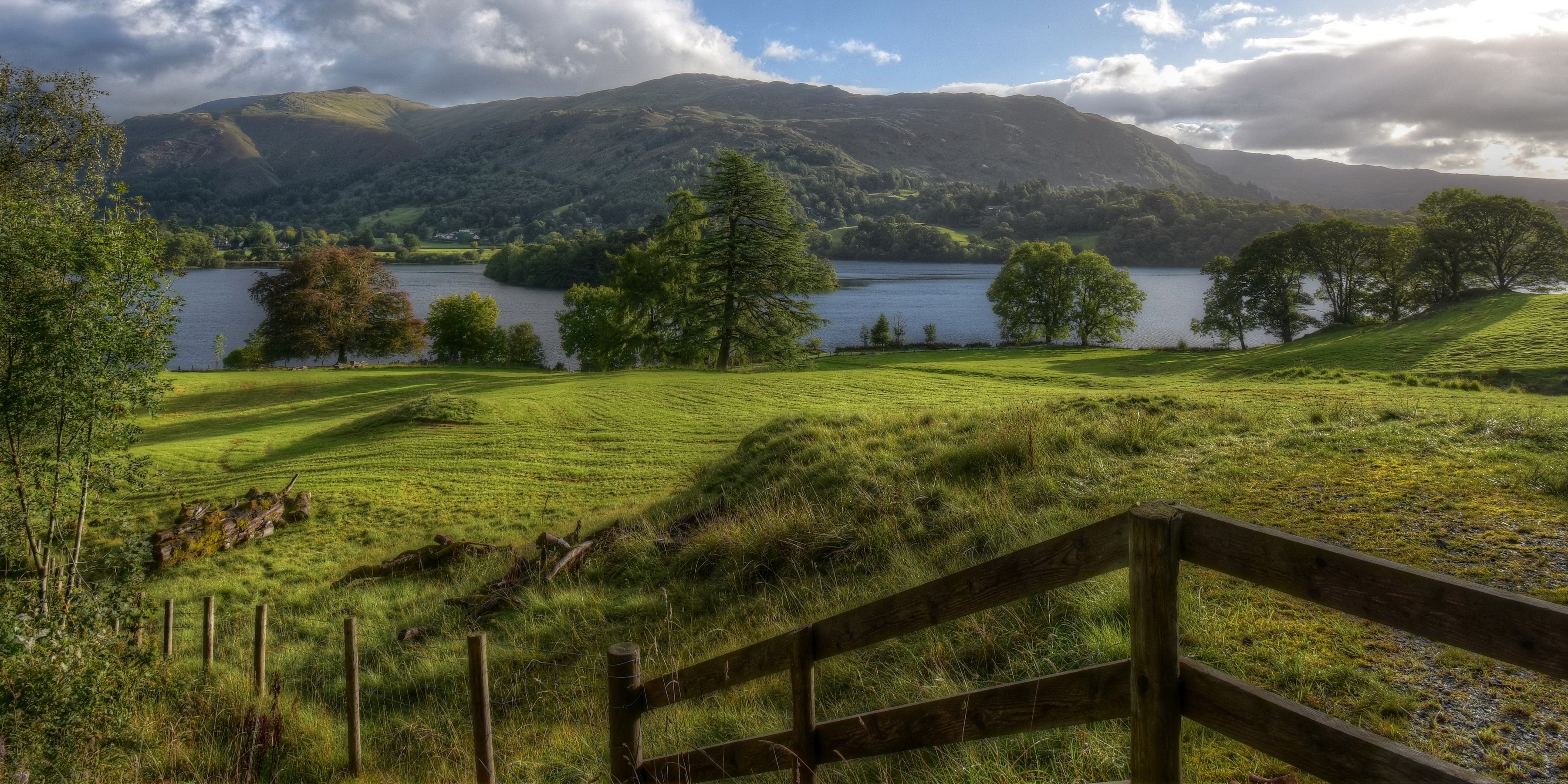 Grassy hillside overlooking a lake and mountains in Cumbria, UK HD Wallpaper