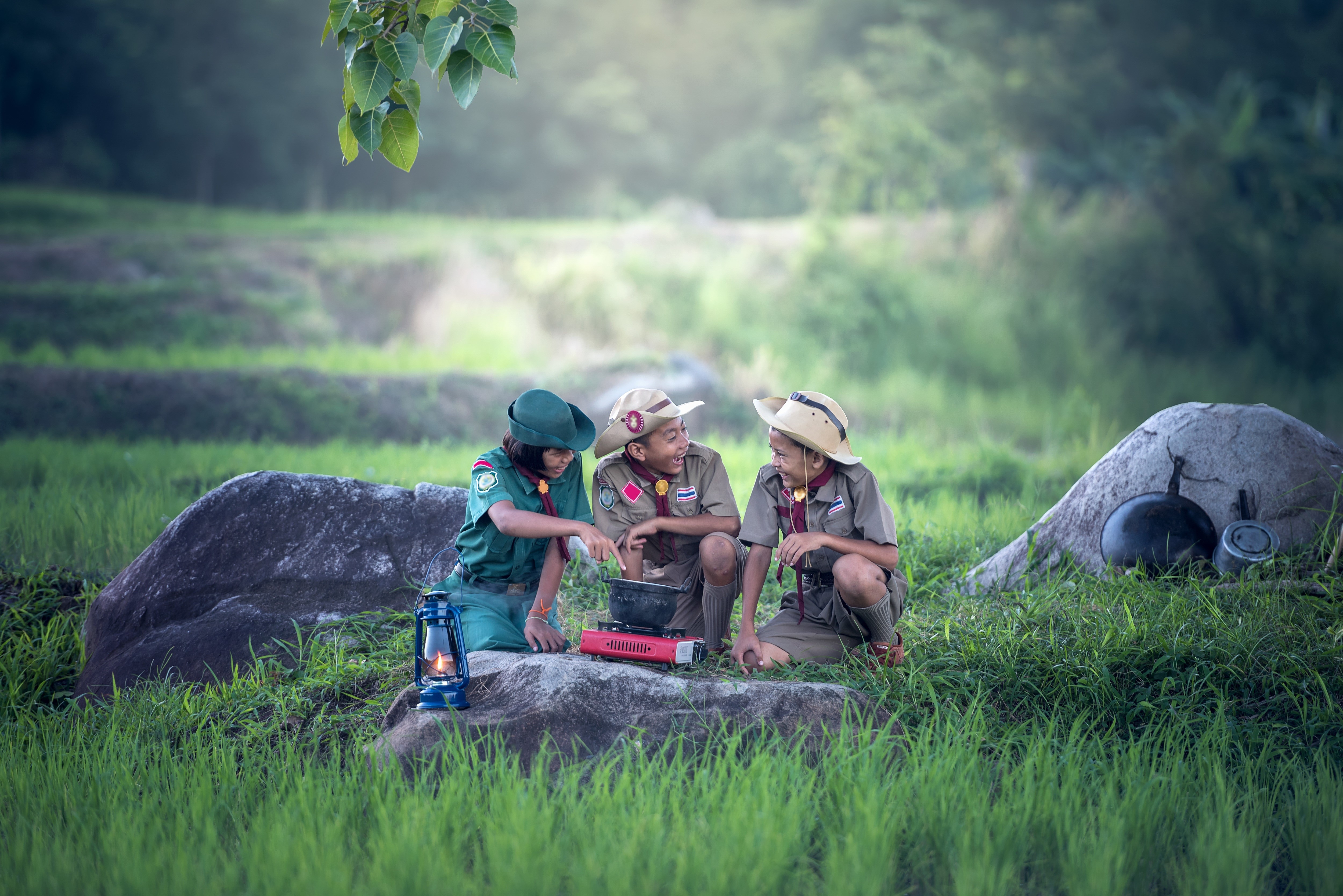 Three scouts cooking outdoors on rocks HD Wallpaper