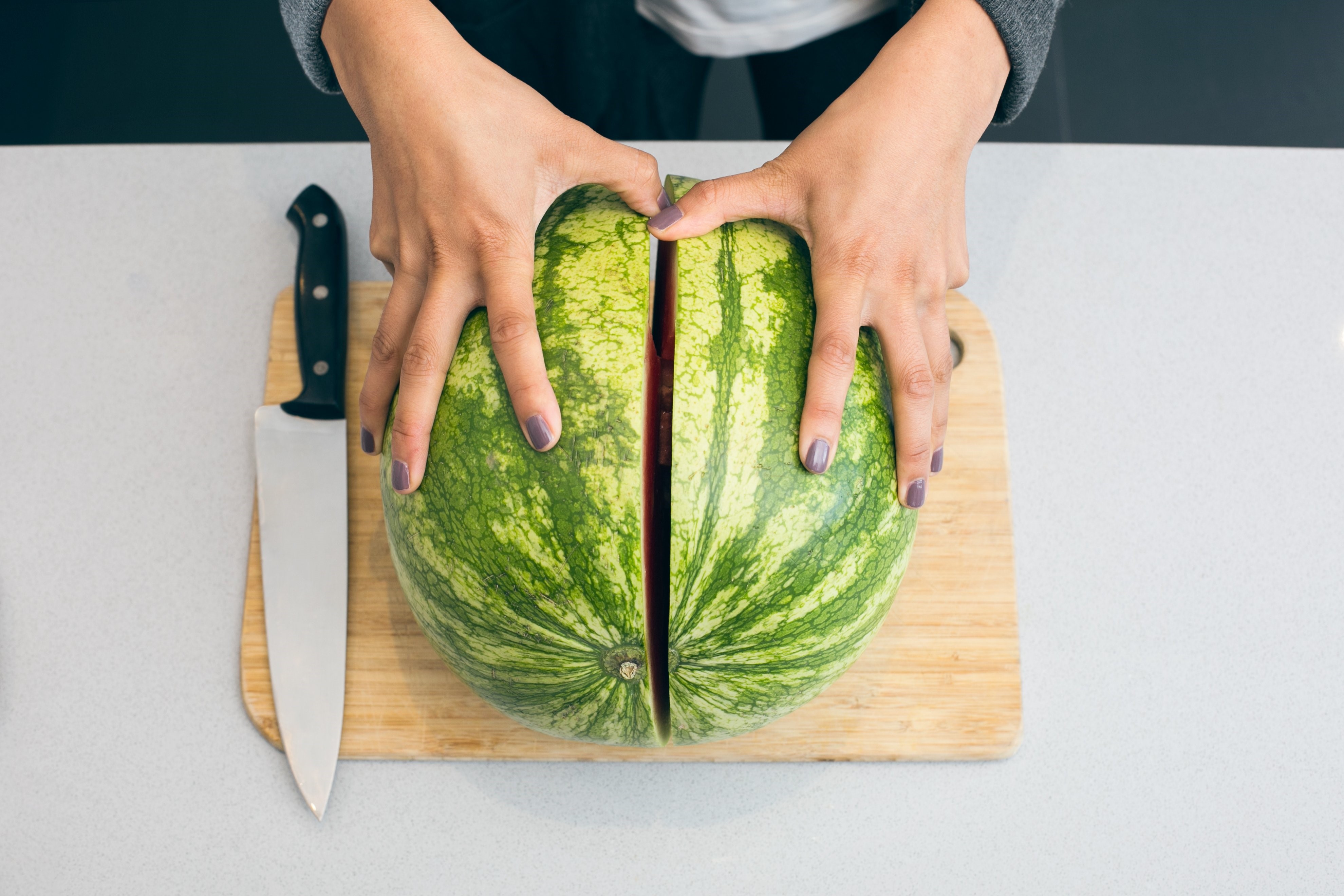 Hands cutting a watermelon with a knife on a cutting board HD Wallpaper