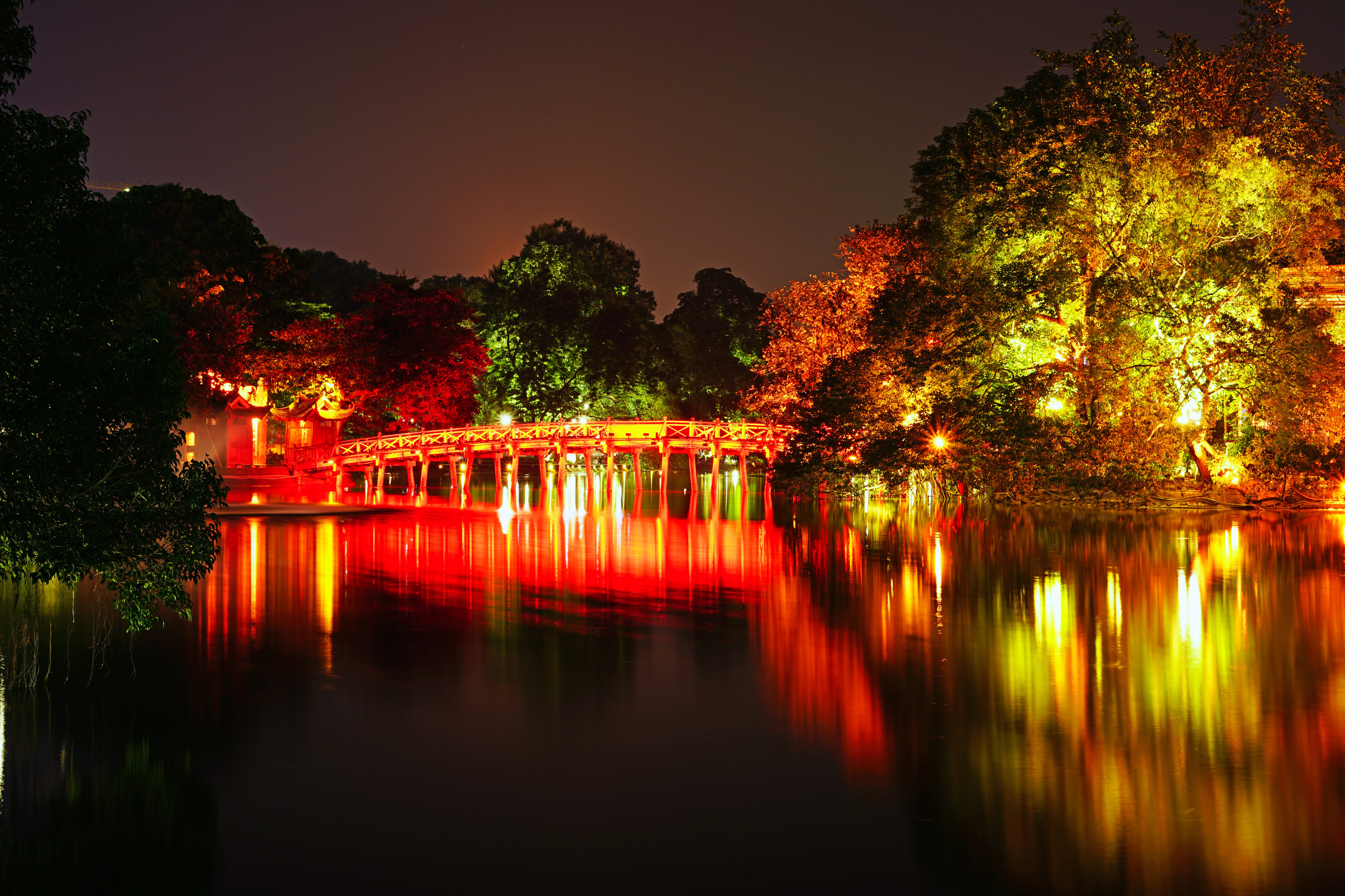Bridge and trees reflected in water at night in Hanoi, Vietnam HD Wallpaper