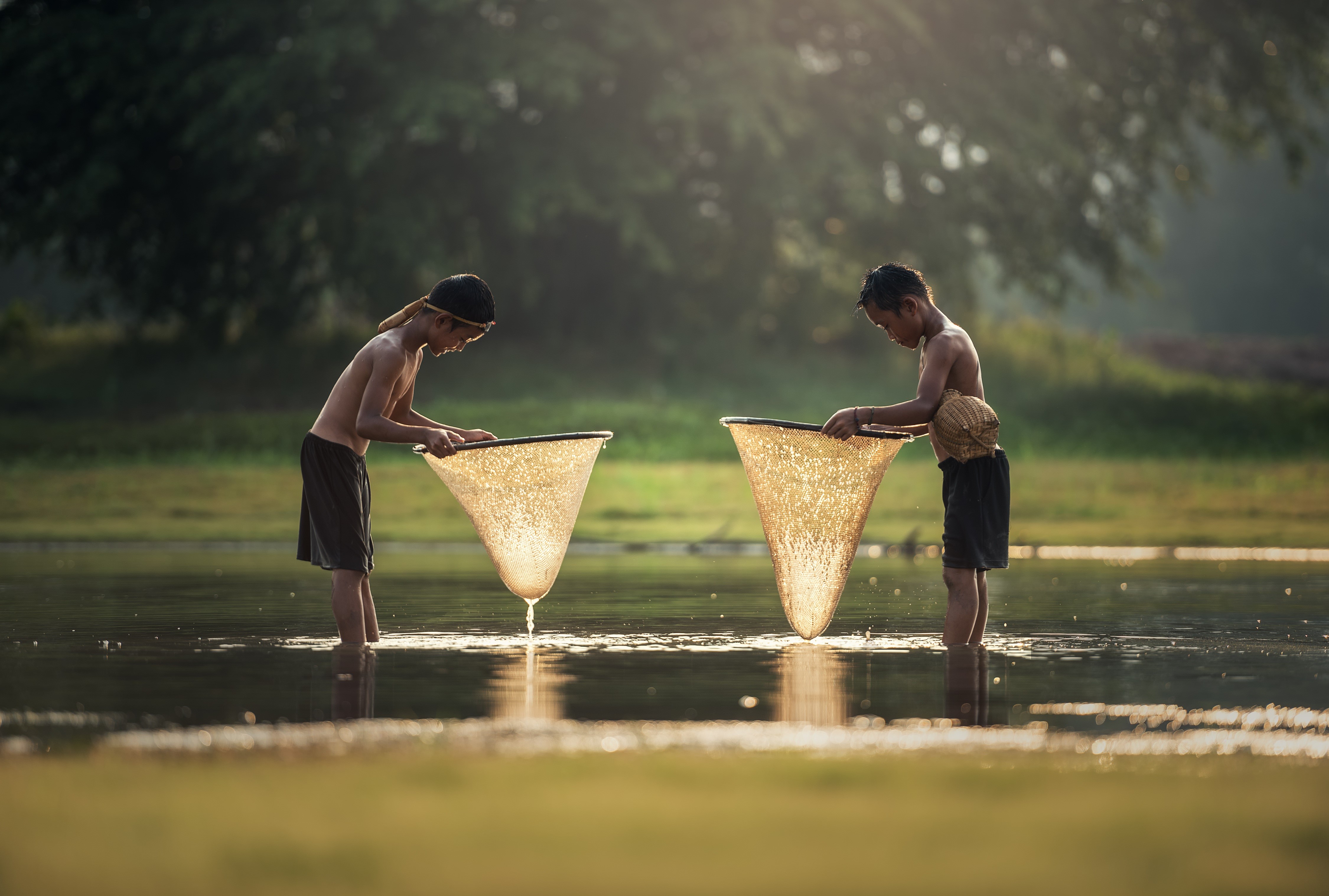 Two Boys Fishing with Nets in Sunlit Water HD Wallpaper