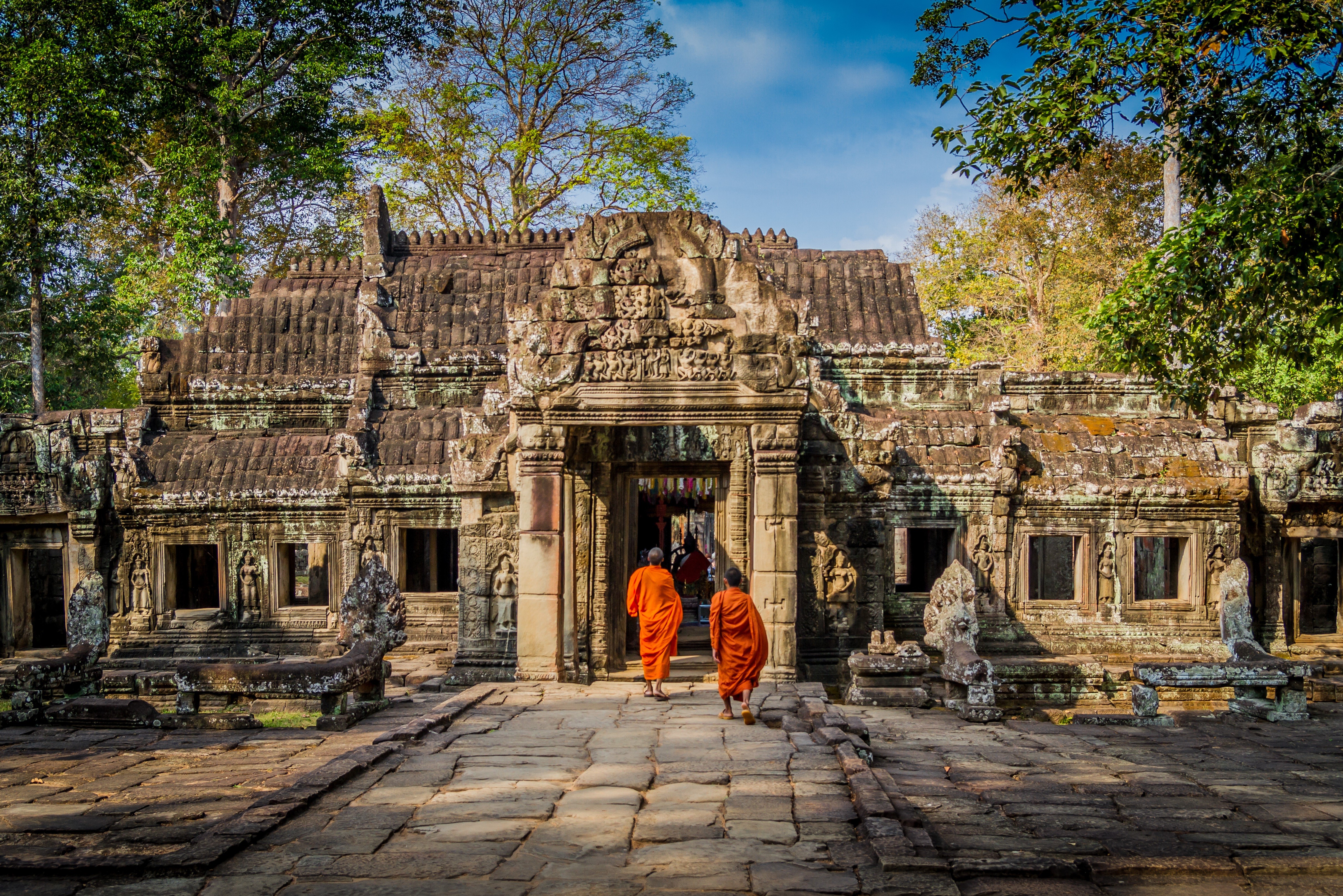 Two monks walk towards ancient temple entrance in Cambodia HD Wallpaper