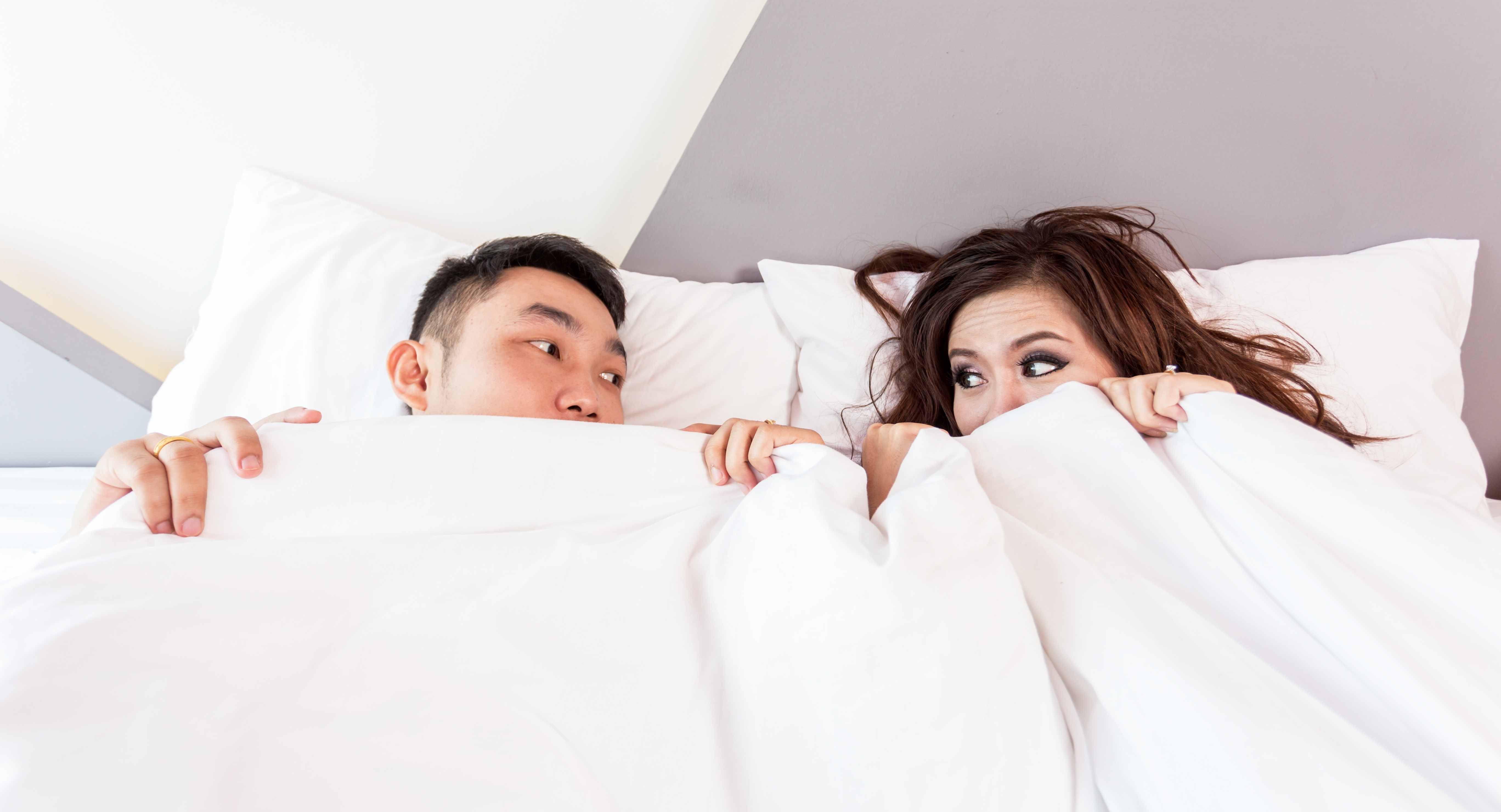 Couple peeking from under the covers in bed HD Wallpaper