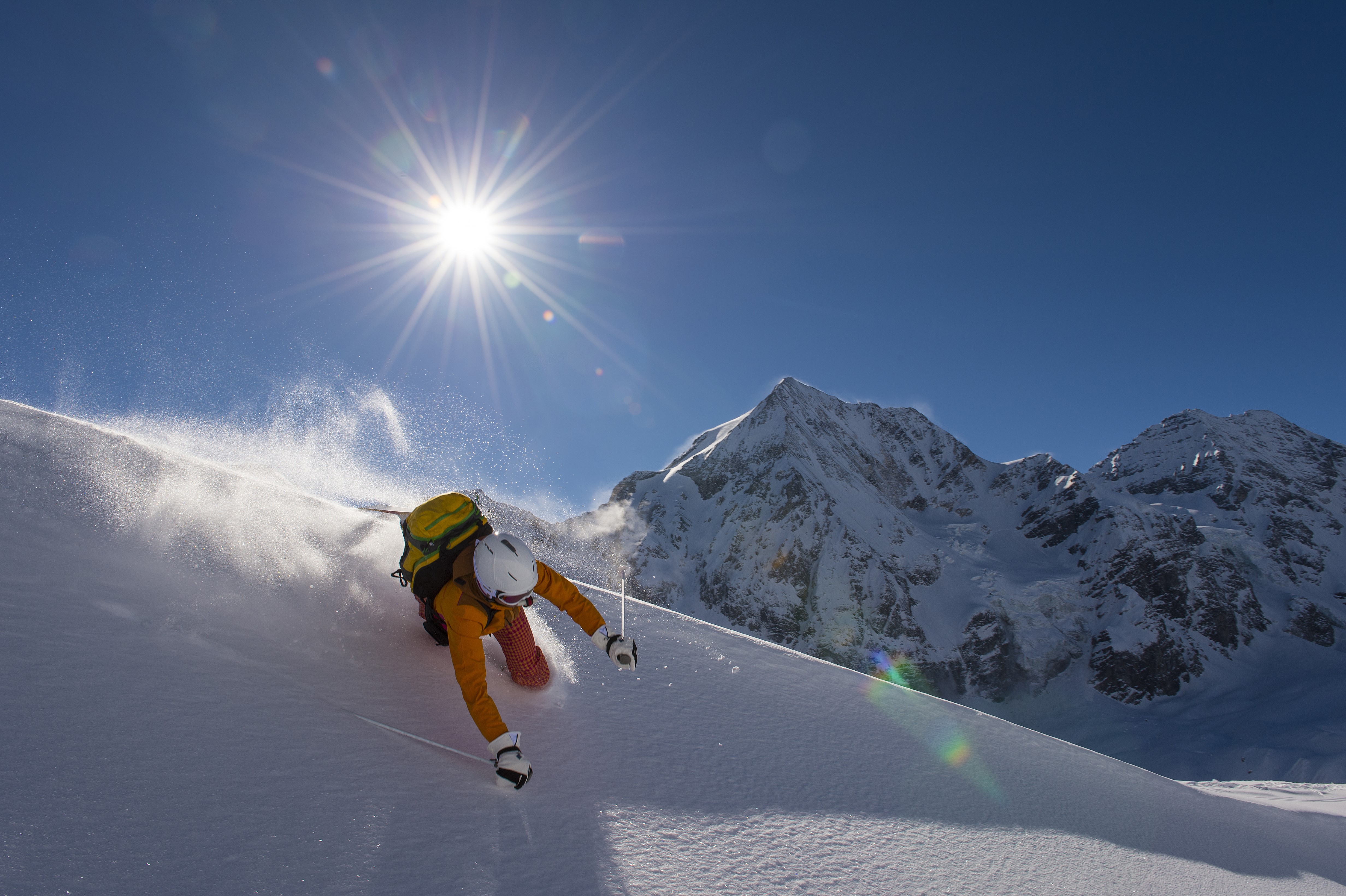 Man skiing down a snowy mountain under the sun HD Wallpaper