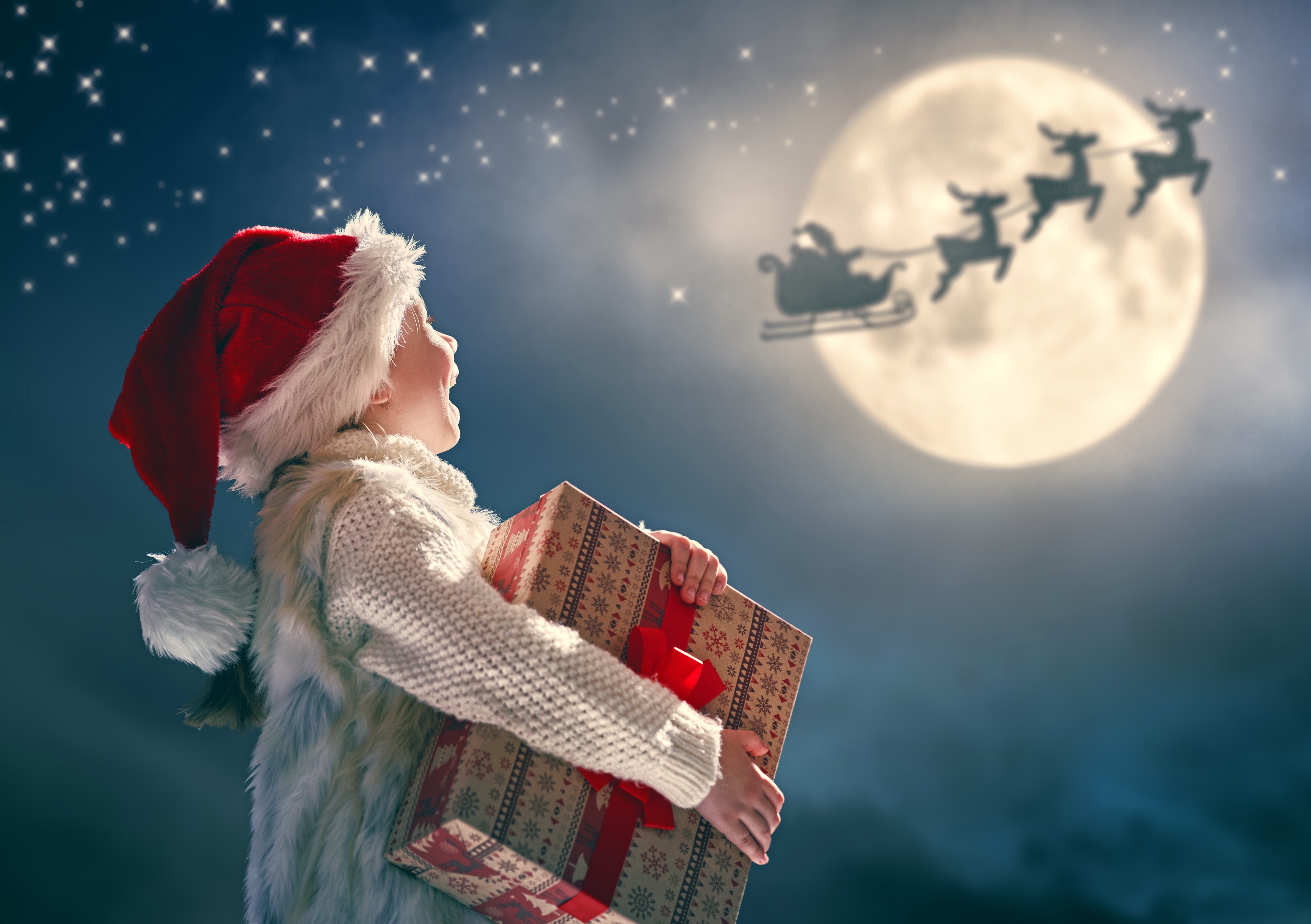 Child with Christmas gift looking at Santa's sleigh HD Wallpaper