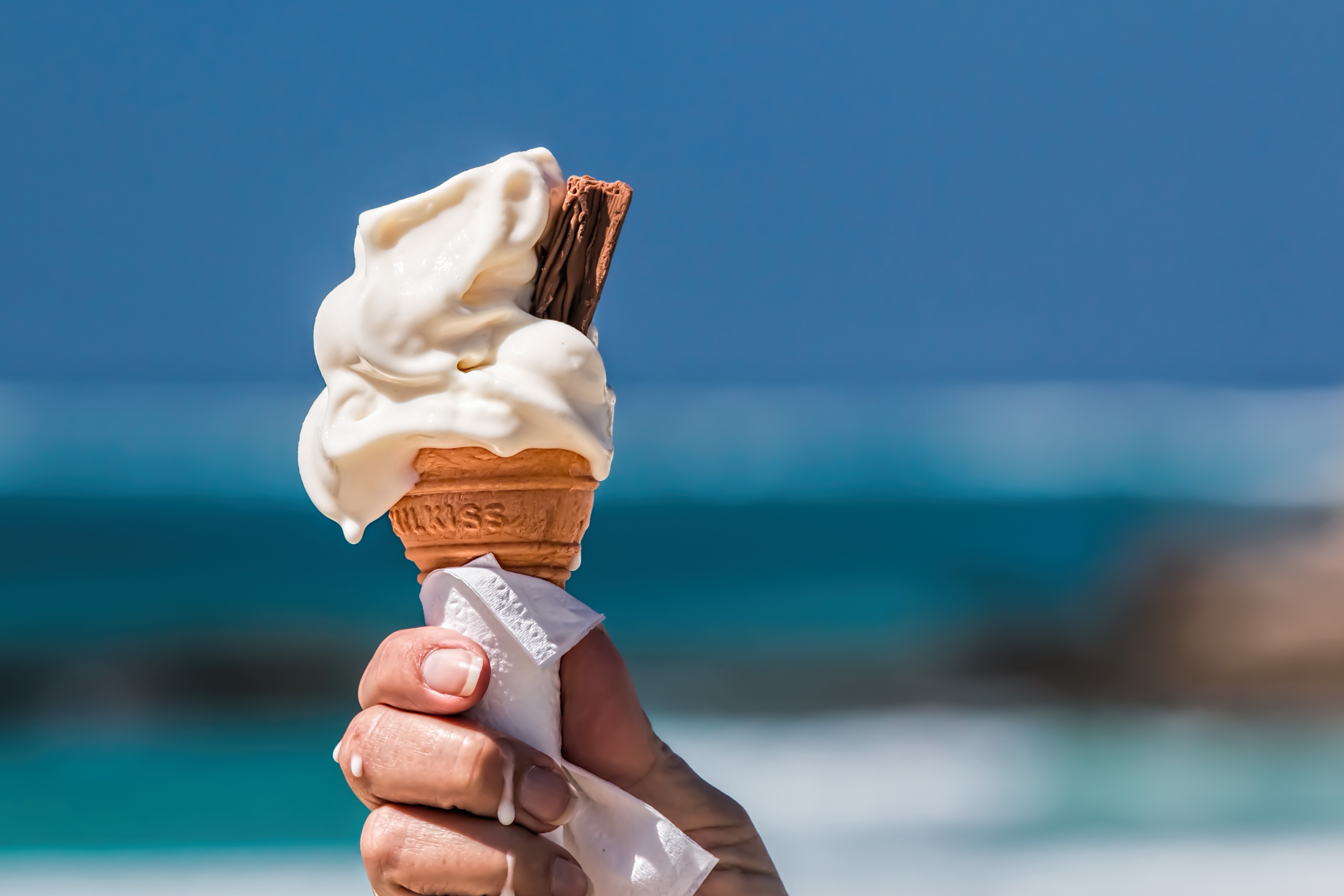Hand holding melting ice cream cone at the beach HD Wallpaper