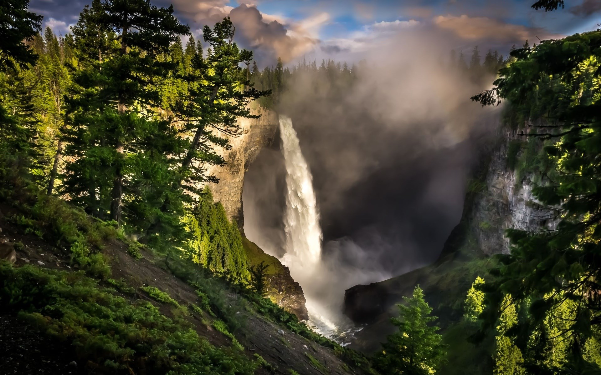 Waterfall cascading into a misty canyon with evergreen trees HD Wallpaper