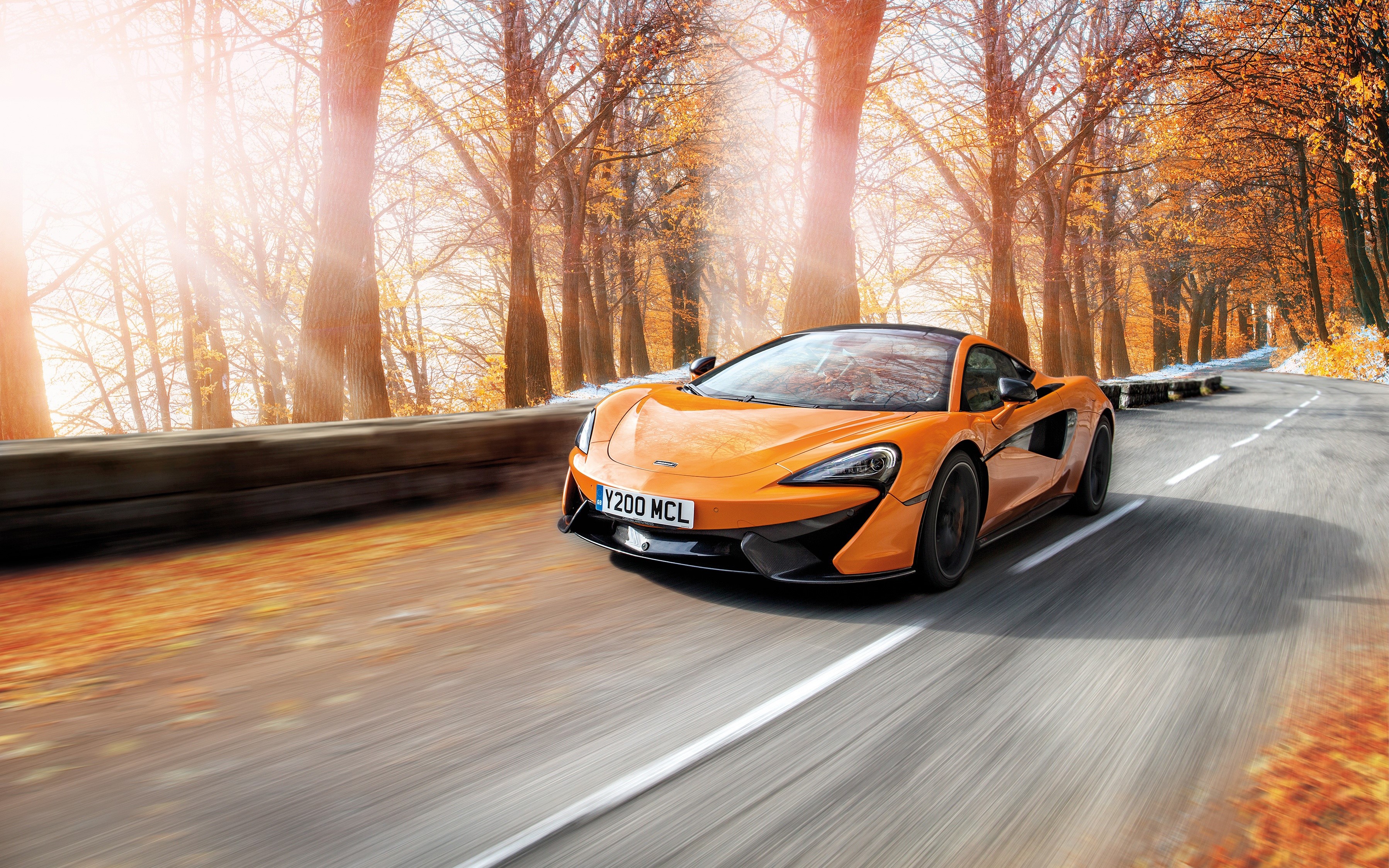 Orange McLaren 570S driving on a road HD Wallpaper