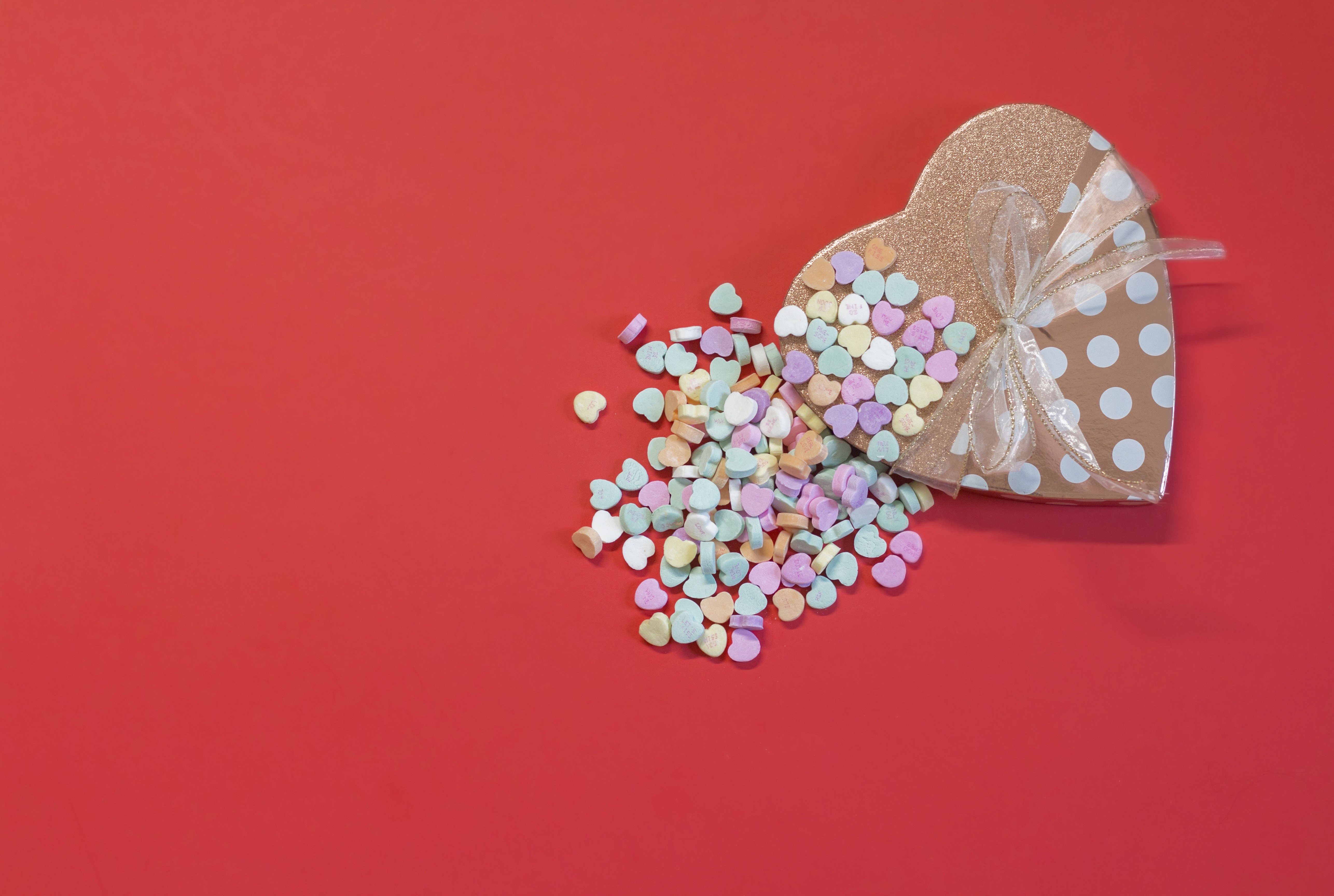 Heart-shaped gift box spilling candies on red background HD Wallpaper