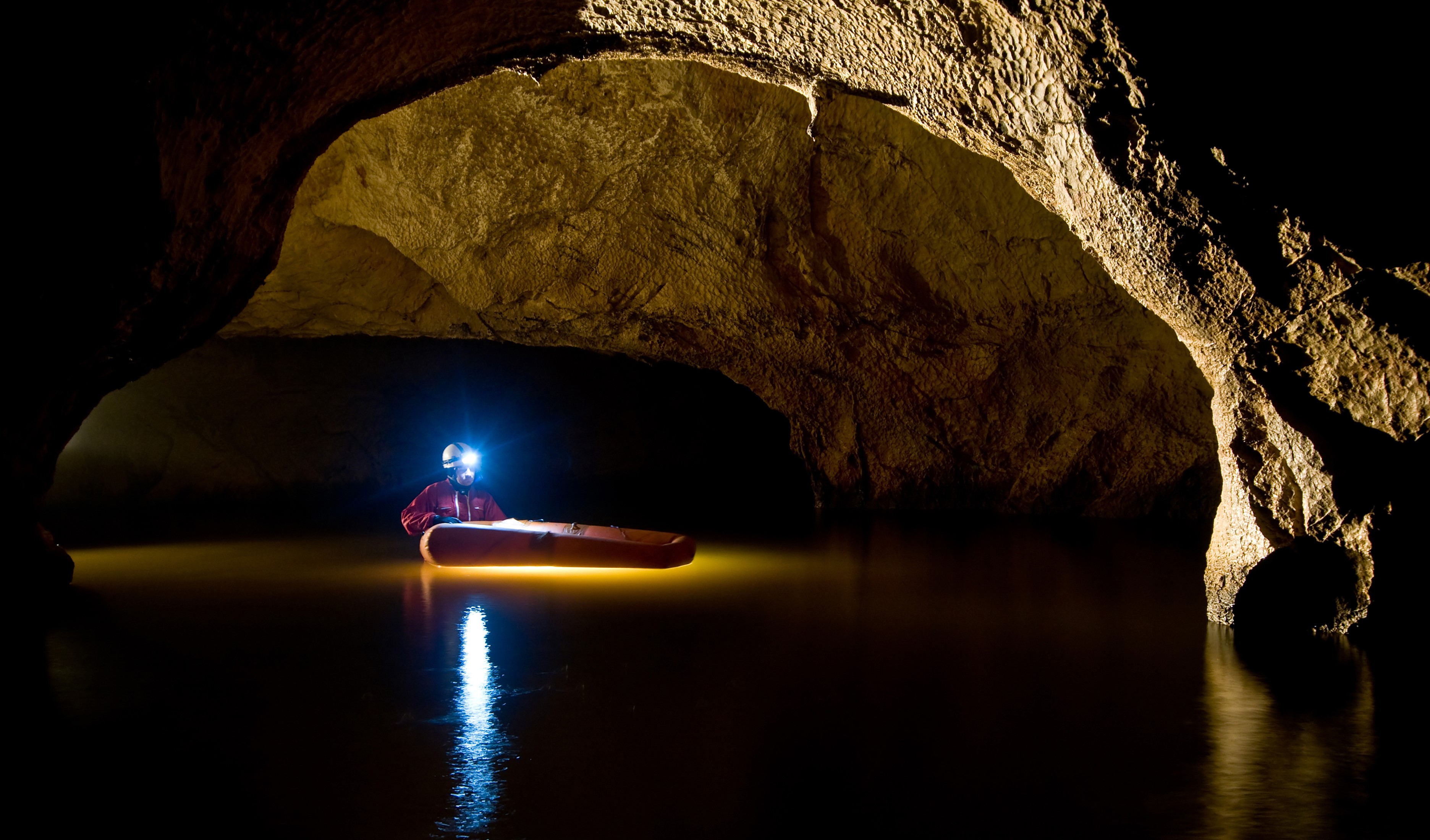 Man in a cave with a headlamp on a boat HD Wallpaper