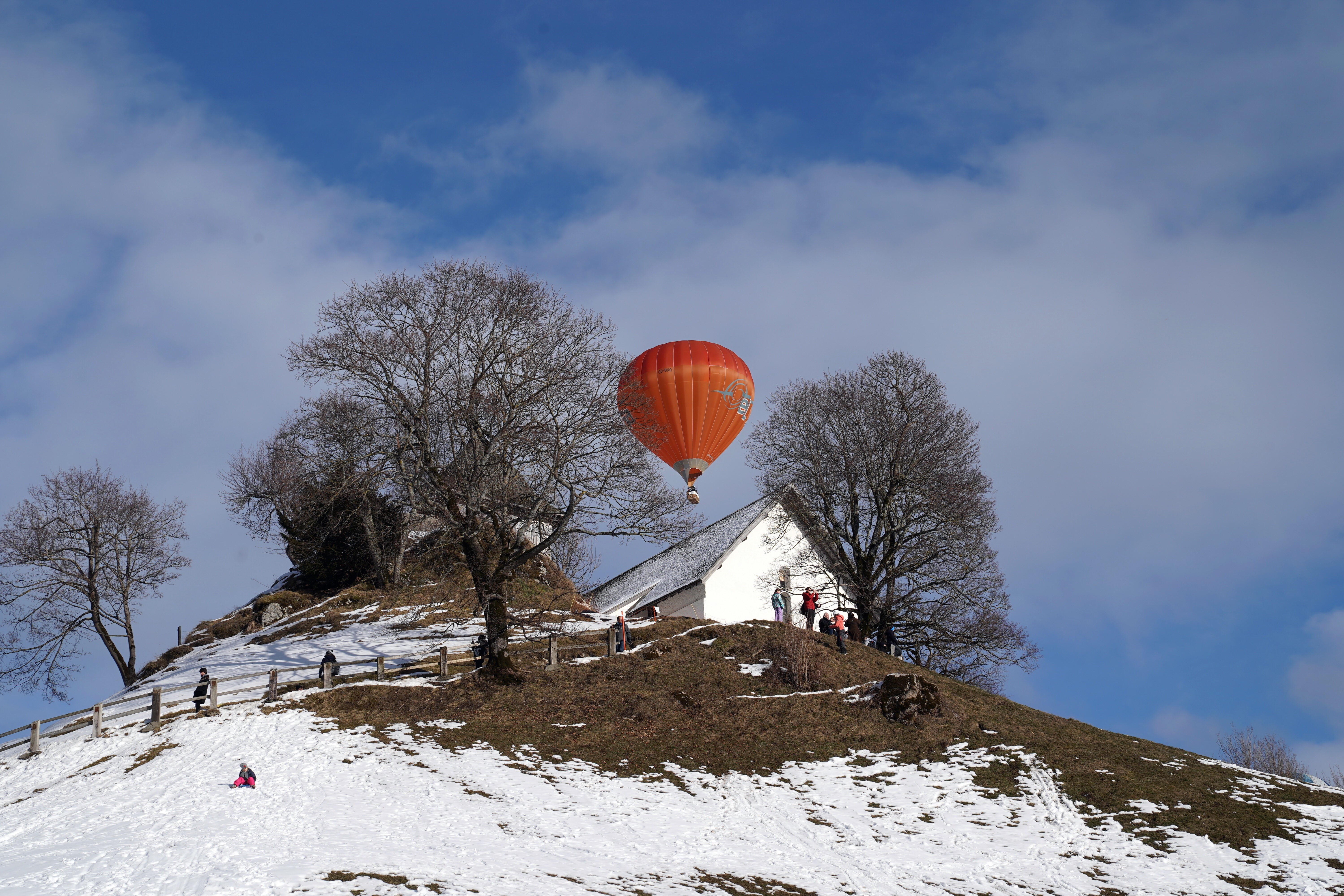 Orange hot air balloon over a snowy hill with a house HD Wallpaper