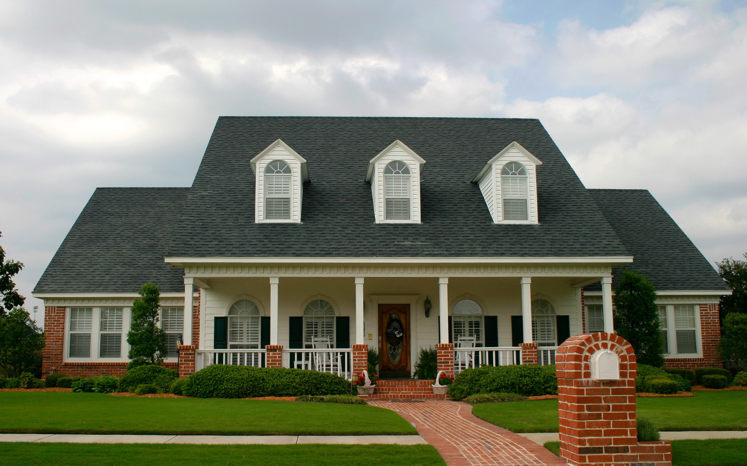 A large brick and white house with a porch and dormer windows HD Wallpaper