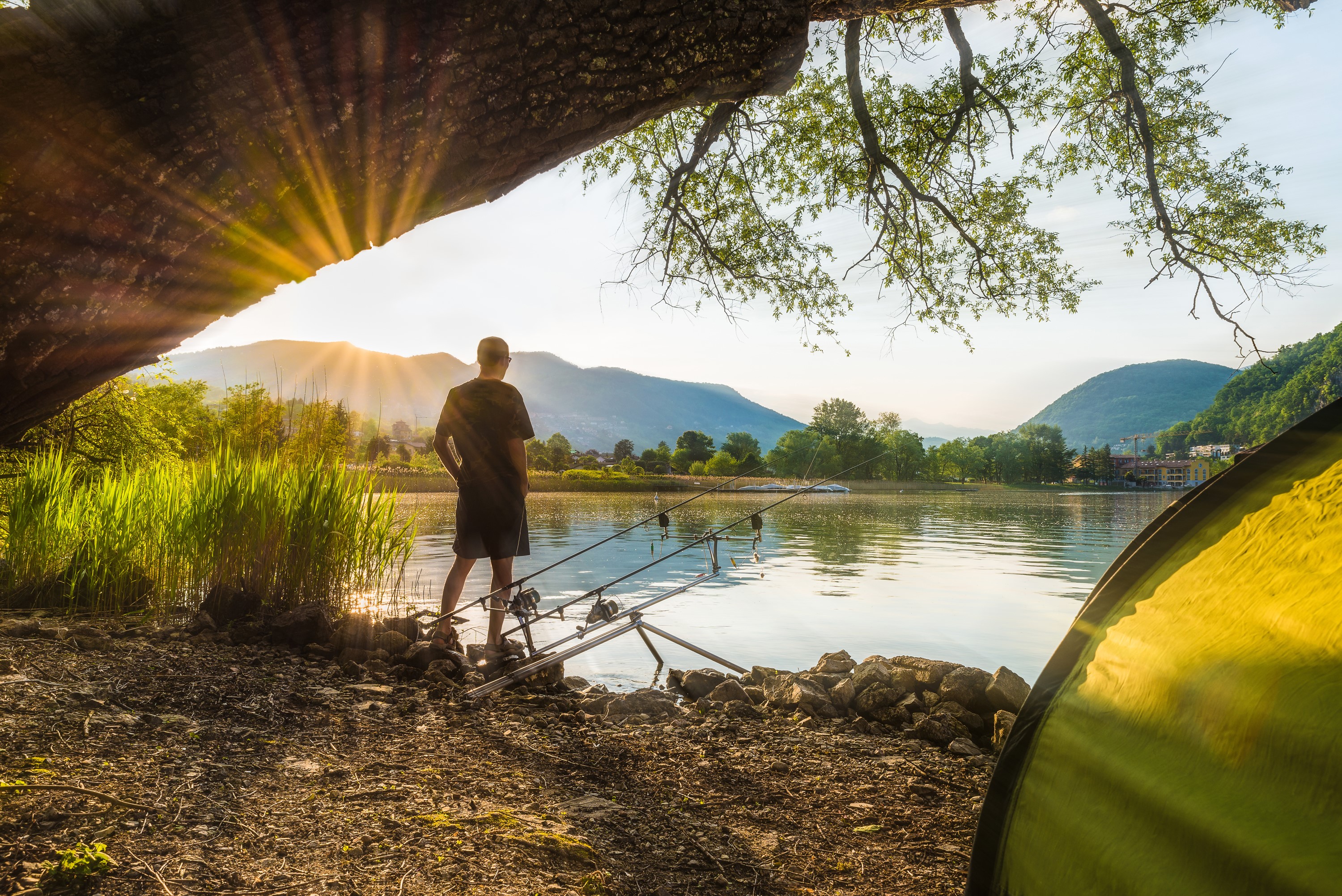 Man fishing by lake at sunrise with tent HD Wallpaper